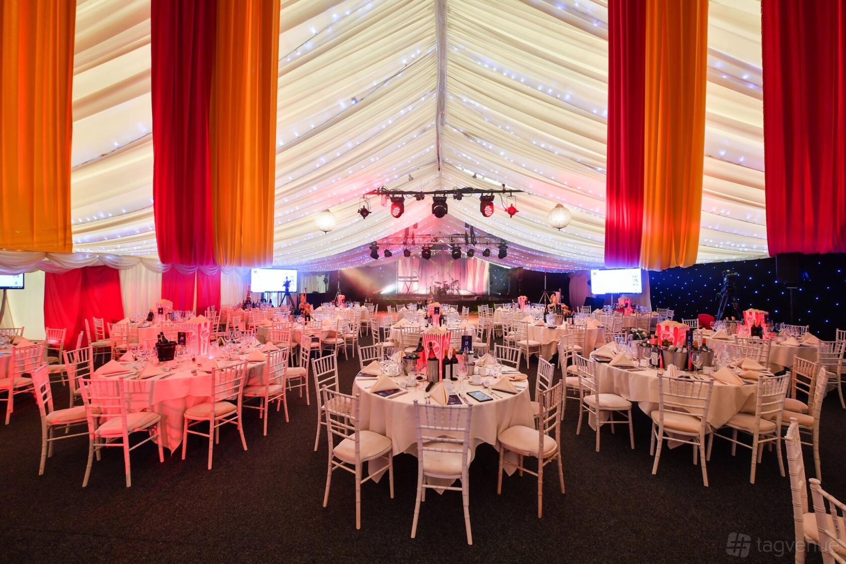 An event space in a hotel with draped fabric ceiling, round tables with white linens, and stage lighting at Coombe Abbey.