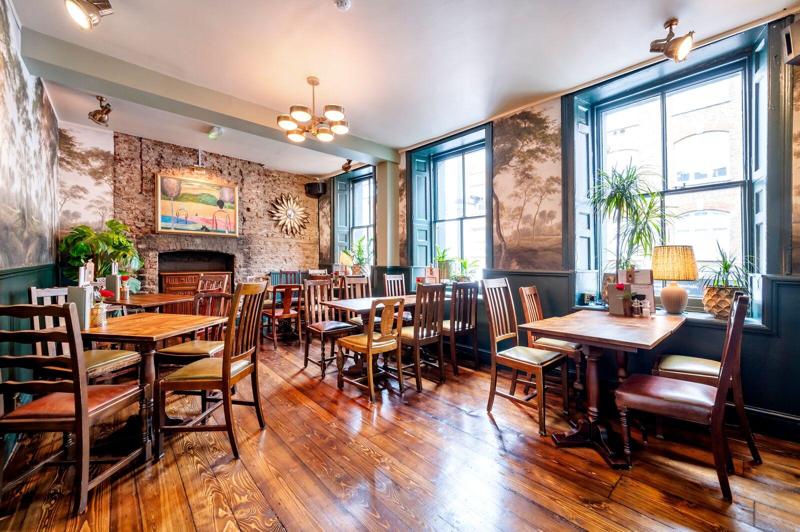 A function room with large sash windows, wooden floors, and assorted wooden tables at The Prince of Wales Feathers.