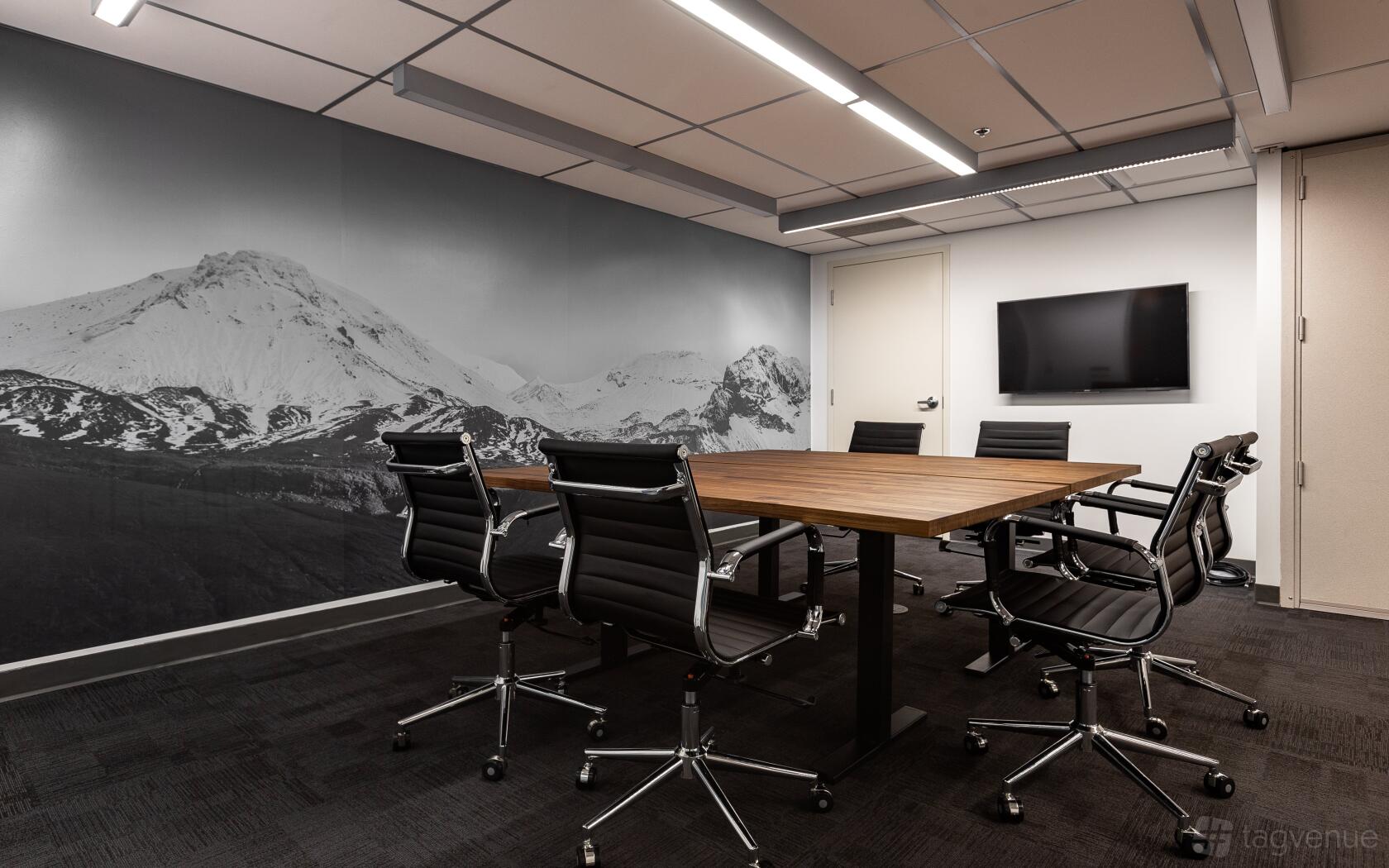A meeting room with a wood conference table, black office chairs, wall-mounted TV, and mountain mural at Adelaide House Coworking.