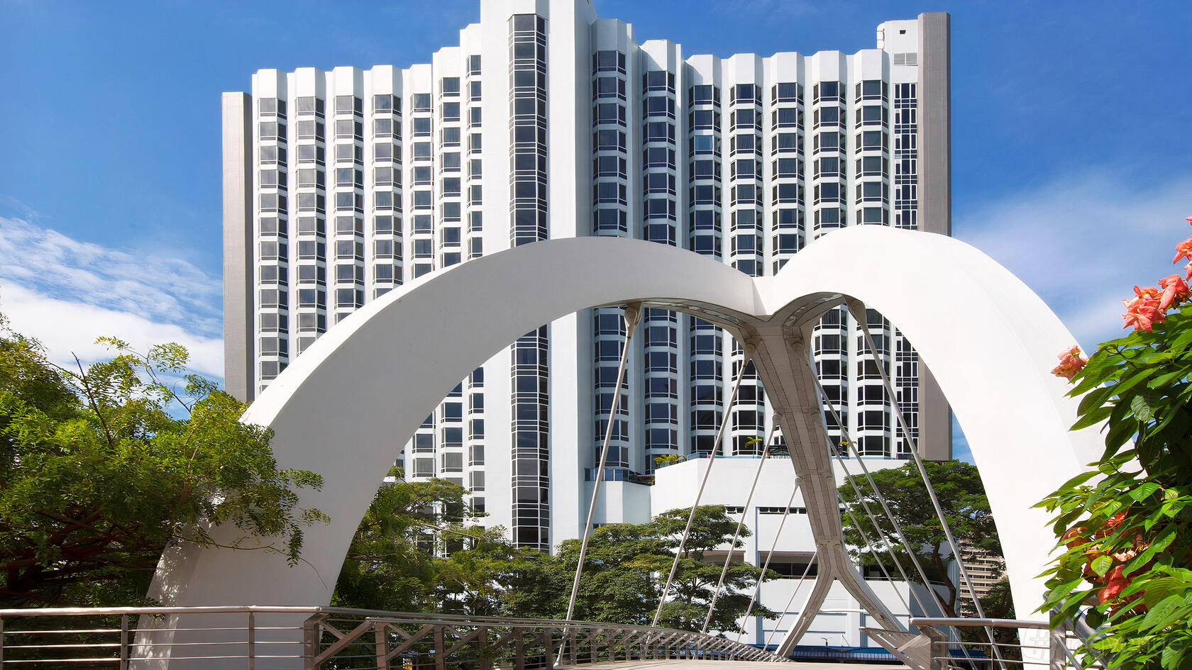 A hotel with a modern white facade and multiple balconies behind a white arched pedestrian bridge at Four Points by Sheraton.