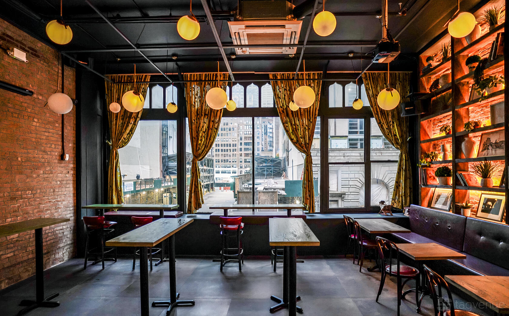 A karaoke bar with tall windows, hanging globe lights, exposed brick walls, and built-in shelving at MS. KIM'S Lounge & Private Karaoke.