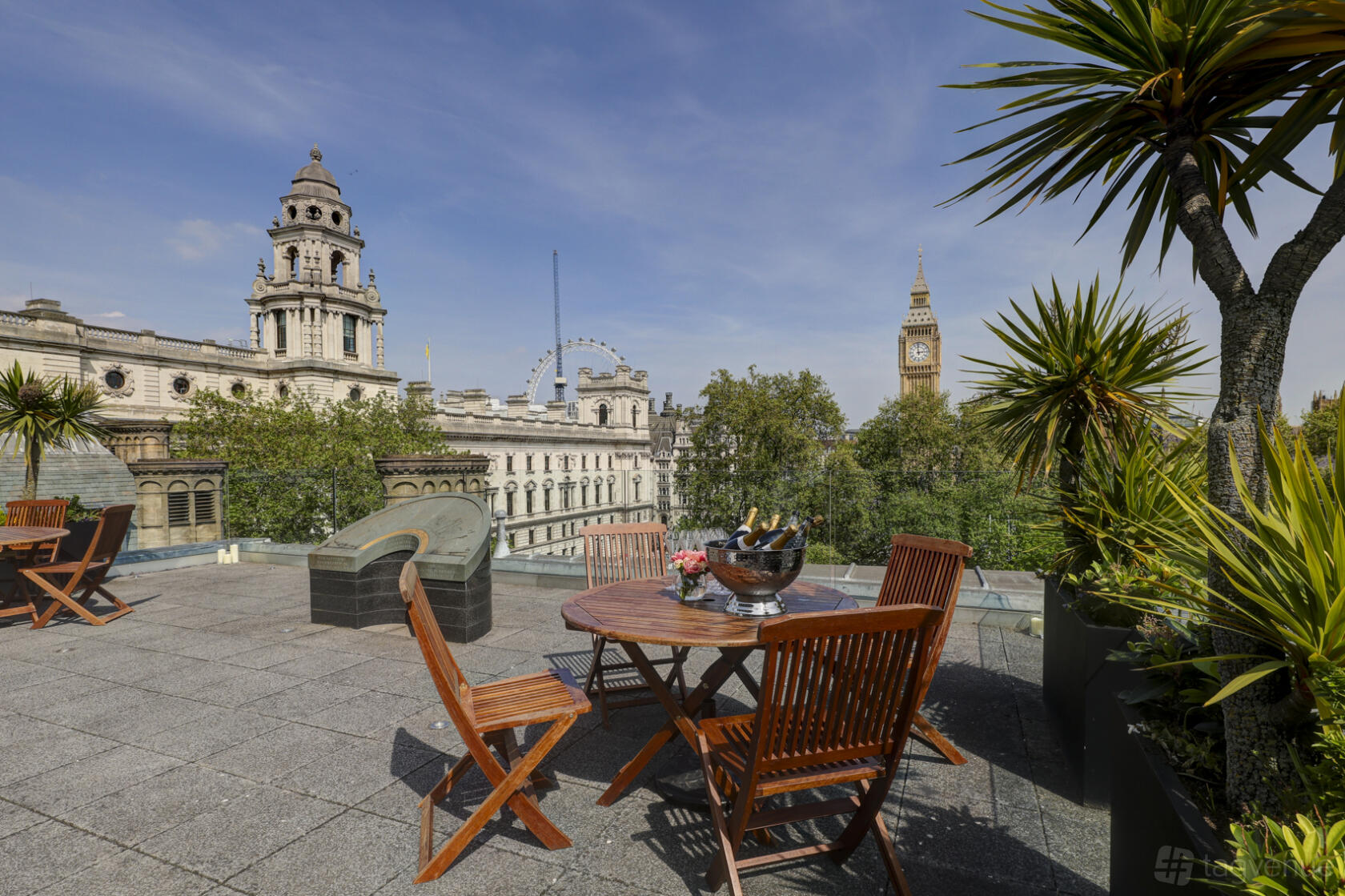A terrace with wooden tables, potted palm plants, and city views including Big Ben at Surveyors House at Rics Westminster.