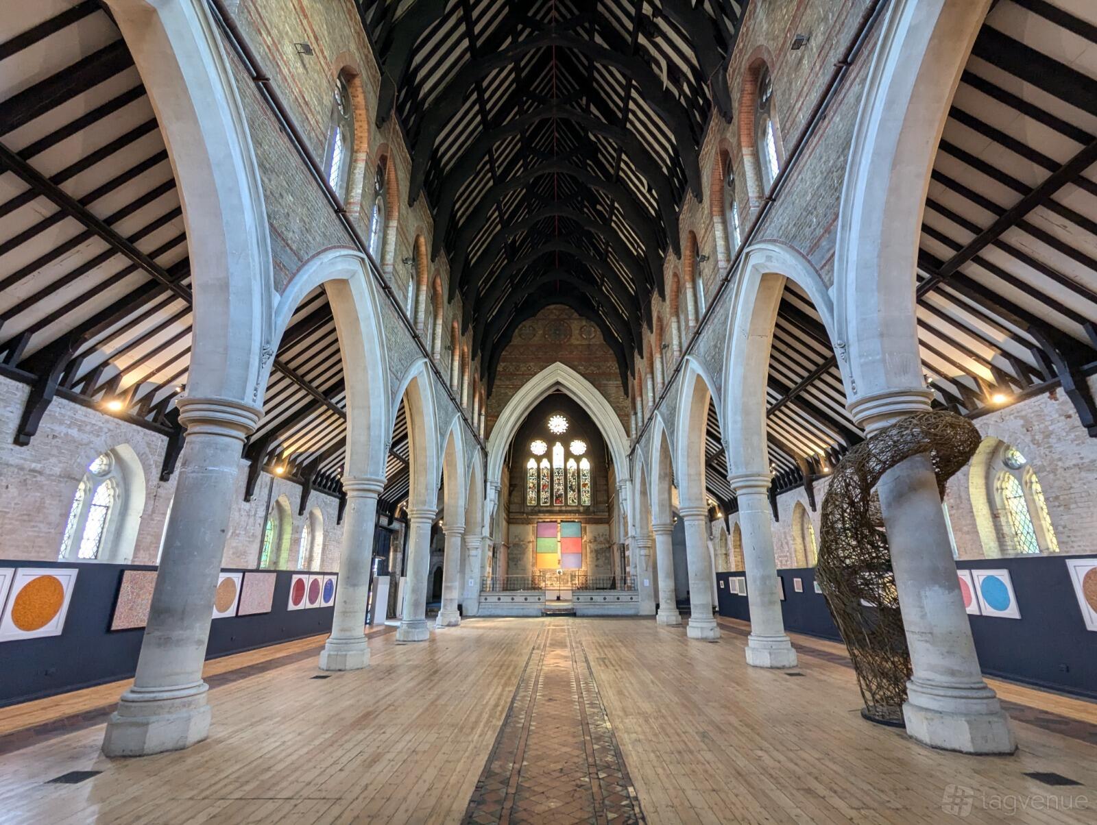 A church interior with high vaulted ceilings, exposed brick walls, arched columns, and stained glass windows at SACRED.