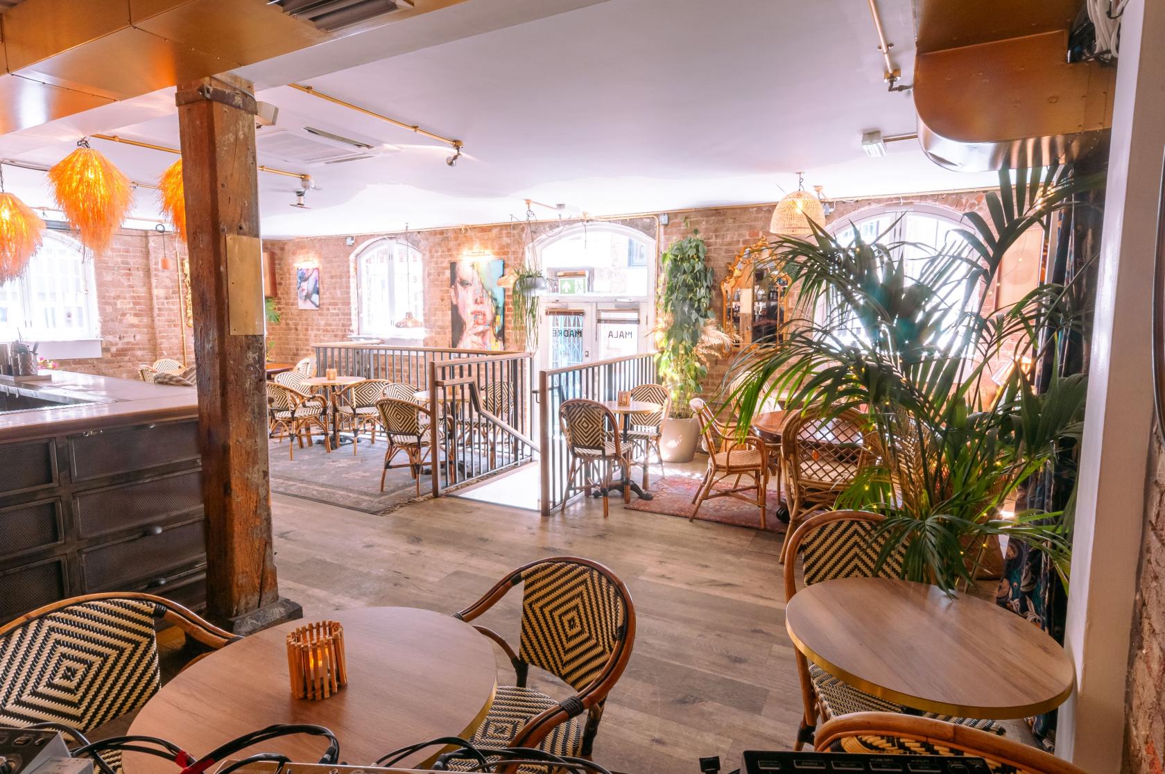 An event space in a restaurant with rattan chairs, exposed brick walls, and large arched windows at The Last Talisman.
