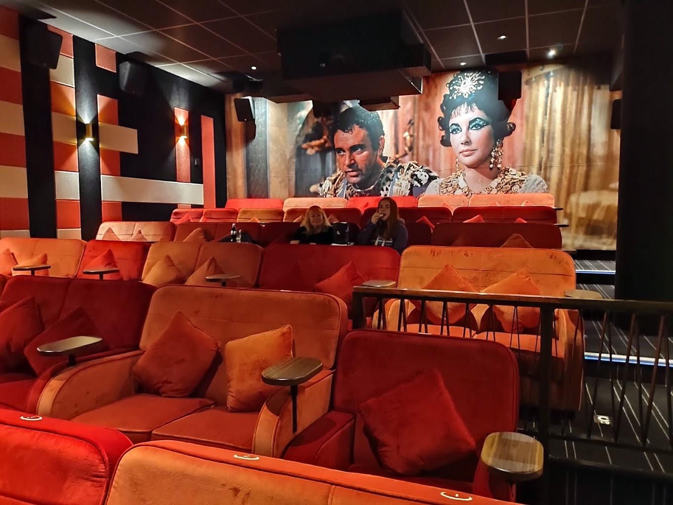 An auditorium with plush red seating, individual armrests, and a classic film mural at Everyman Cardiff.