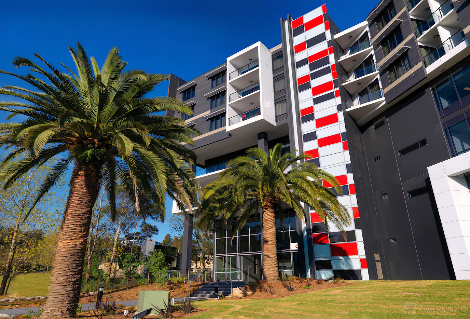 A hotel exterior with geometric red and white facade elements, palm trees, and landscaped grounds at Punthill Norwest.