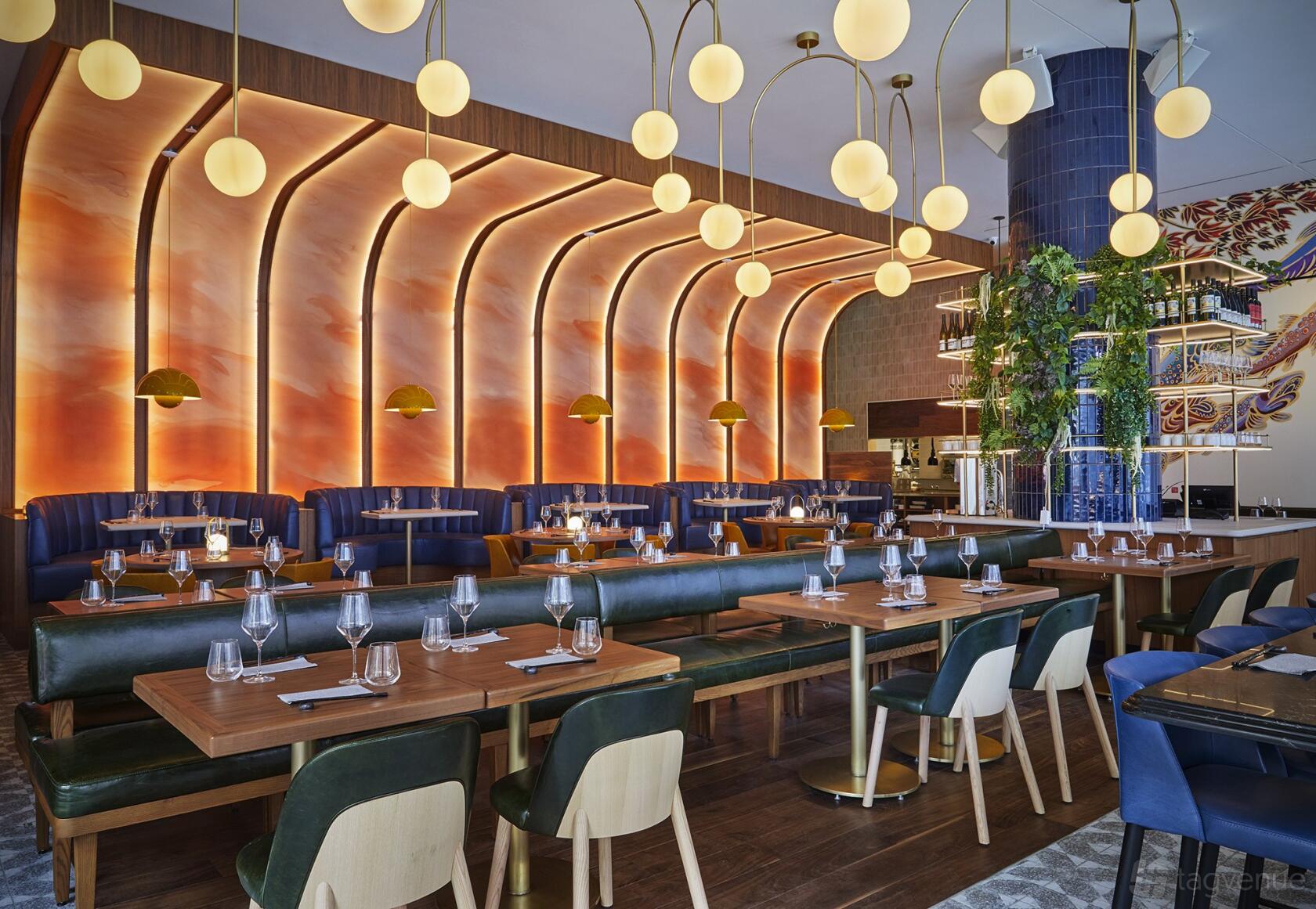 A restaurant with curved amber backlit wall panels, globe pendant lights, and wooden tables at Minami Toronto.