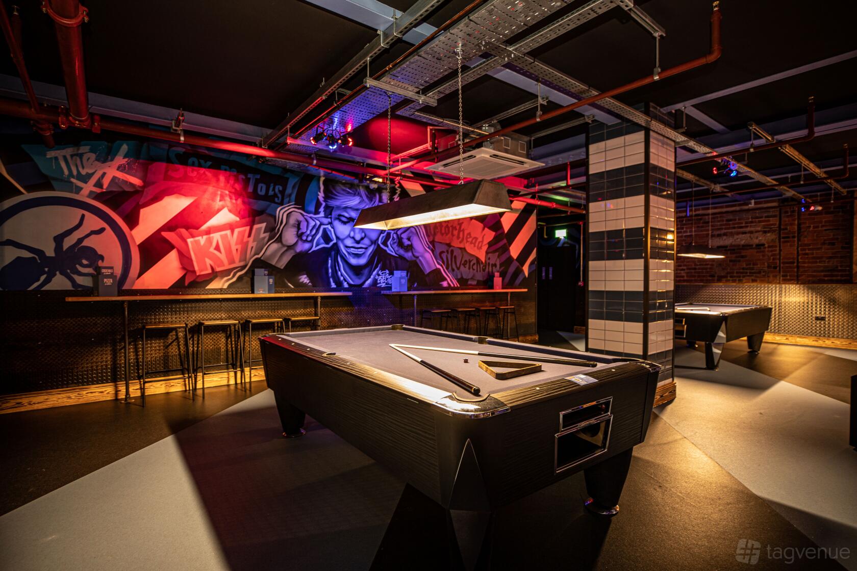An event space in a bar featuring black pool tables, colorful wall murals, and exposed ceiling pipes at Roxy Lanes Leeds The Light.