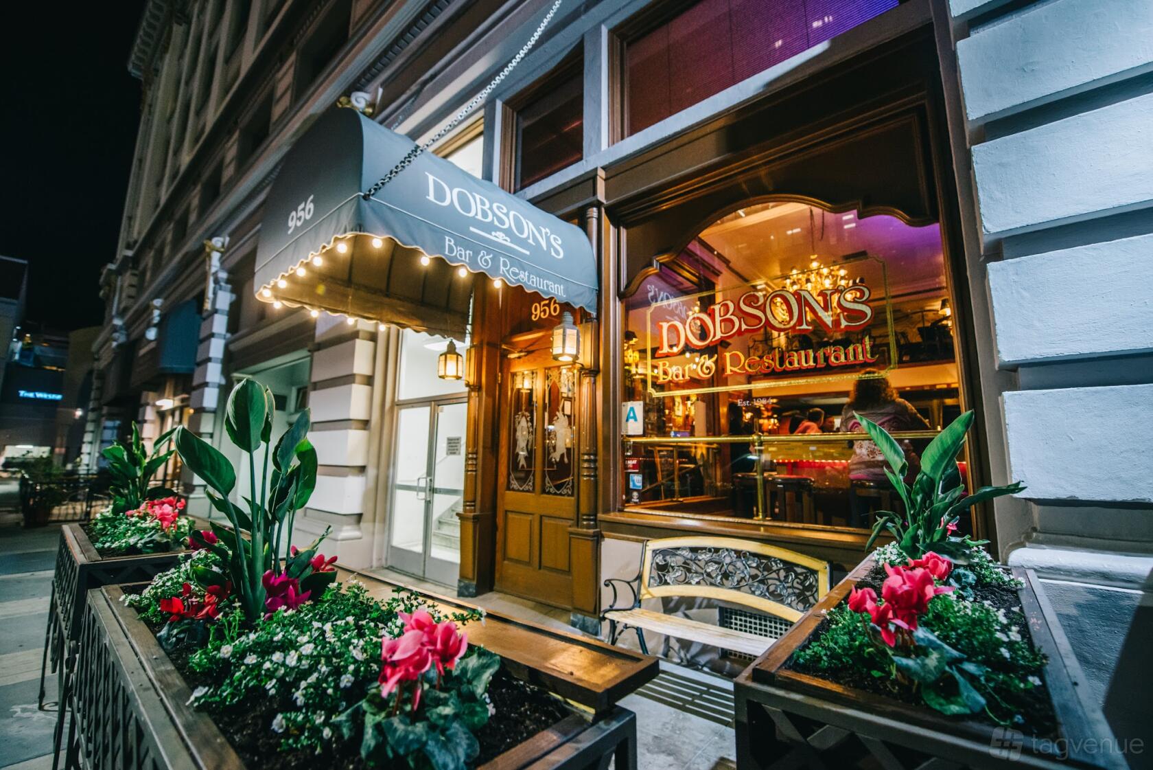 A restaurant exterior with an awning, large window, and flower-filled planters at Dobson's Restaurant.
