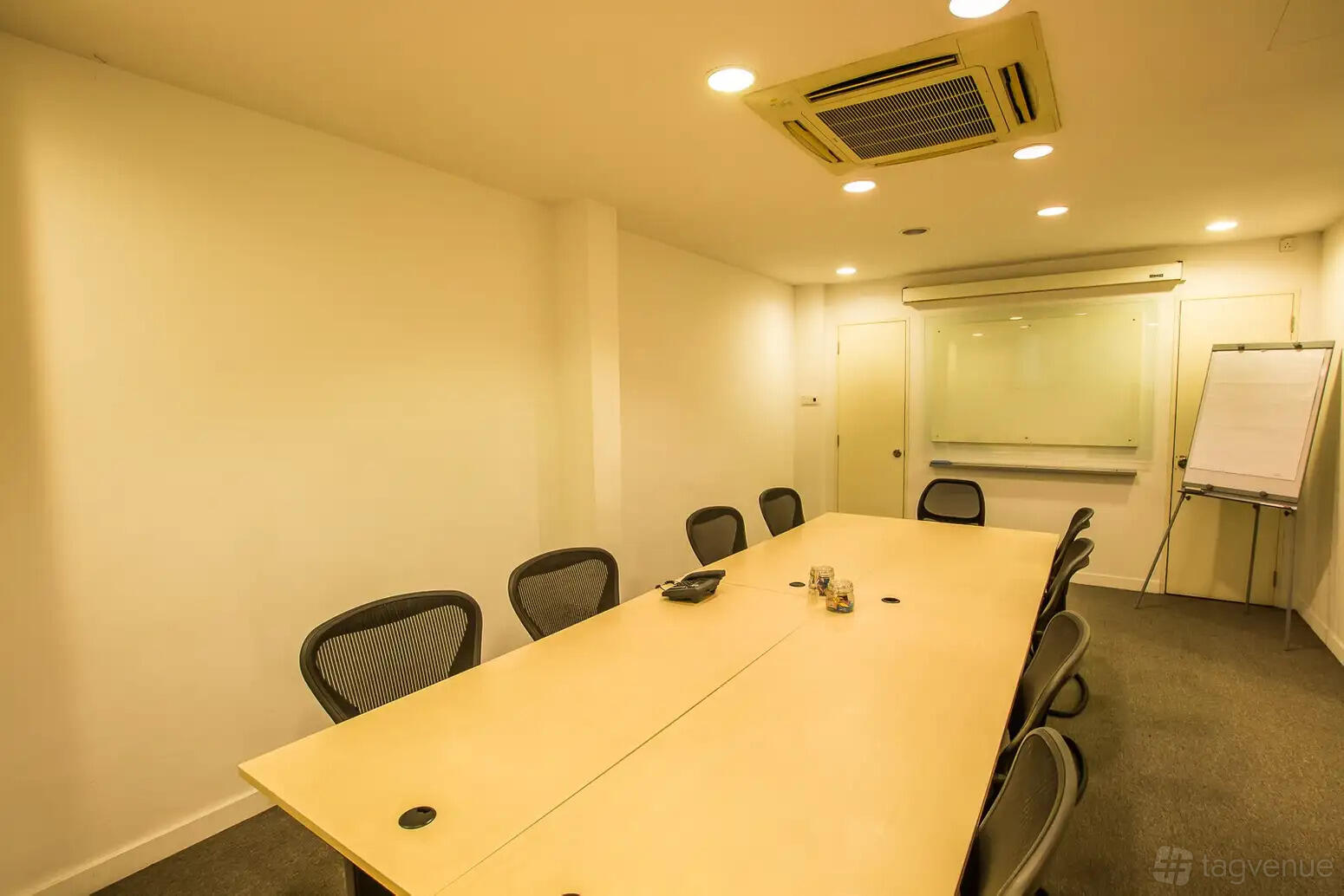 An office space with a long conference table, ergonomic chairs, a glass whiteboard, and flip chart at Signature Space Business Centres.