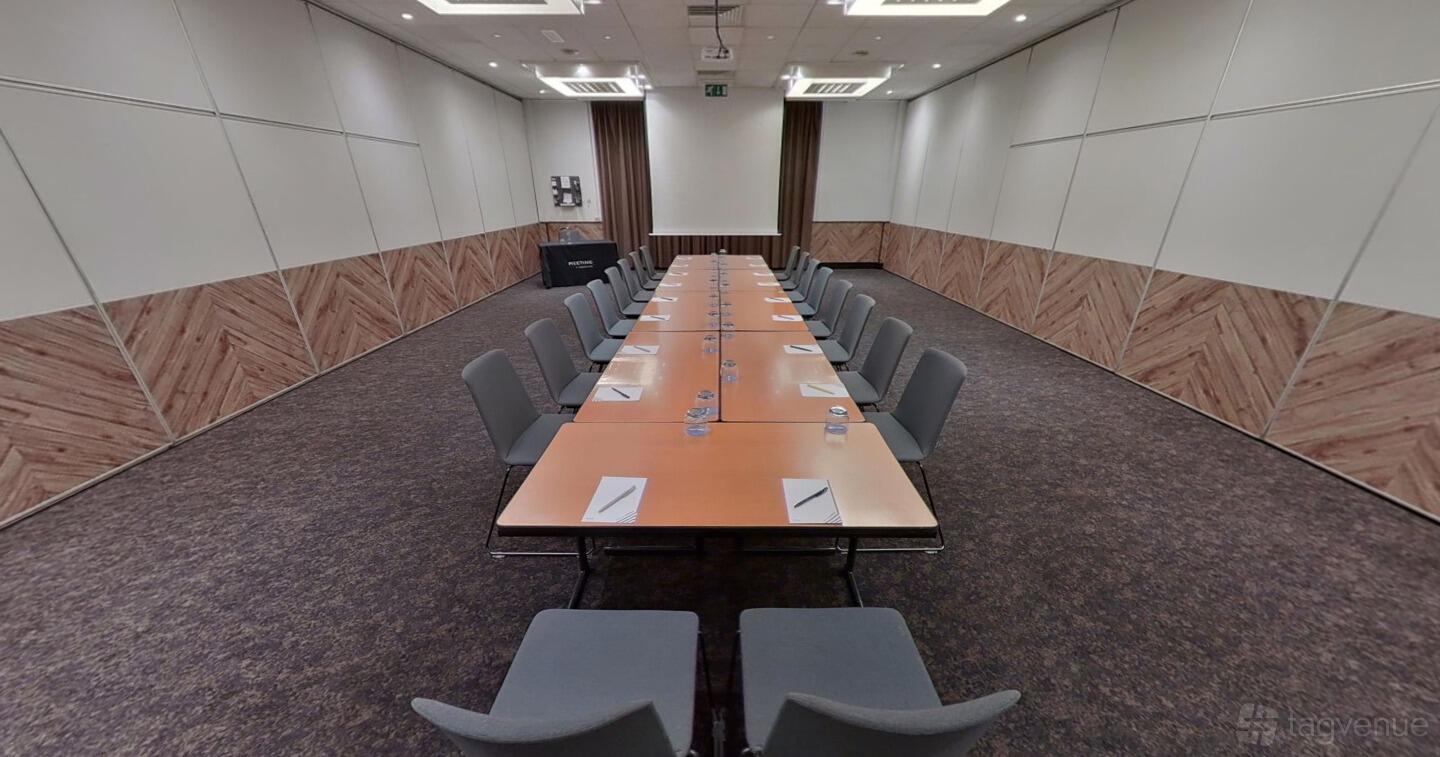 A meeting room with a long rectangular conference table, gray chairs, and wood panel accents at Novotel Birmingham Centre.