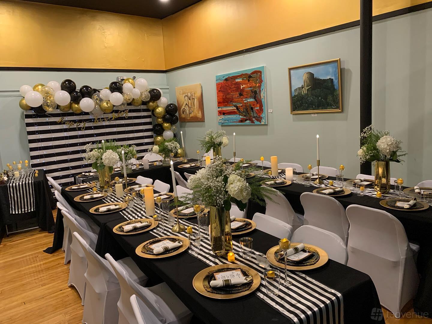 A function room with banquet tables set with gold plates, striped runners, floral centerpieces, and a black-and-gold balloon display at Orchid 7 Fusion Bar & Grill.