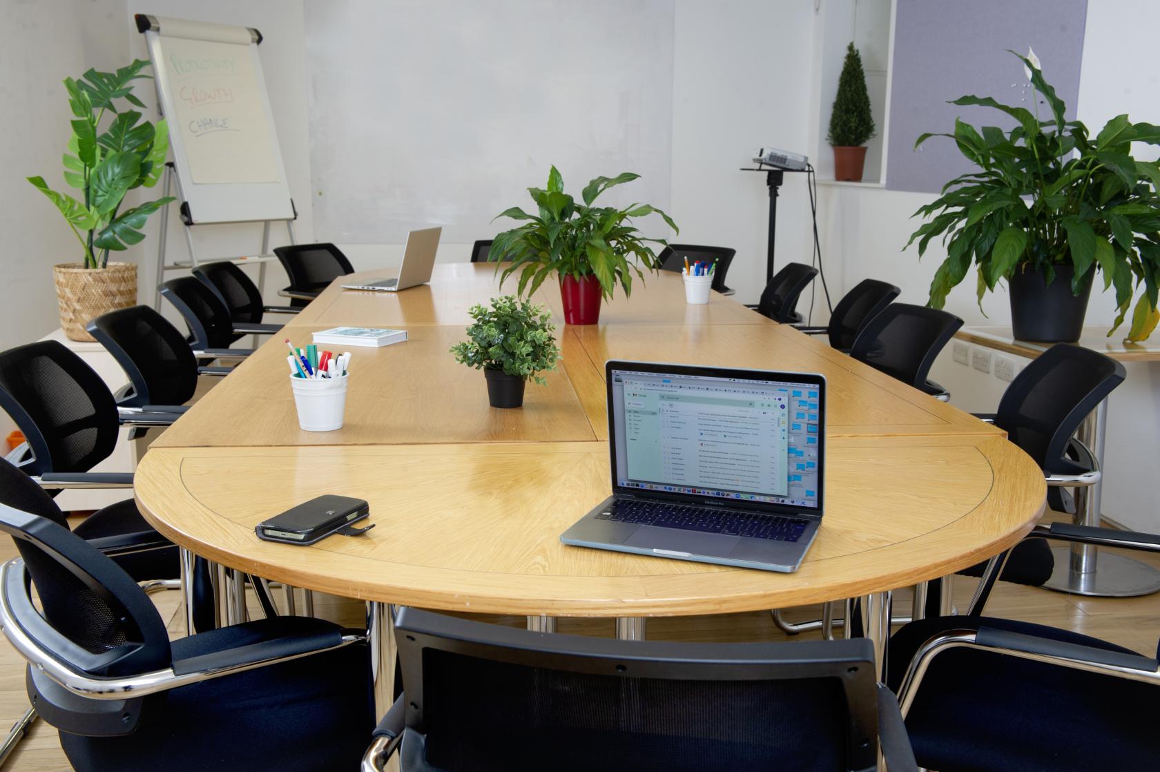 A training room with a large oval table, black chairs, greenery, and a flipchart at The Melting Pot.
