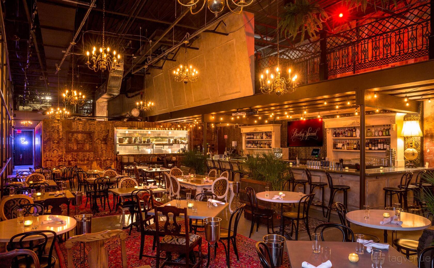 A restaurant with chandeliers, vintage chairs, round tables, and a long bar under warm lighting at Bootleg Special.
