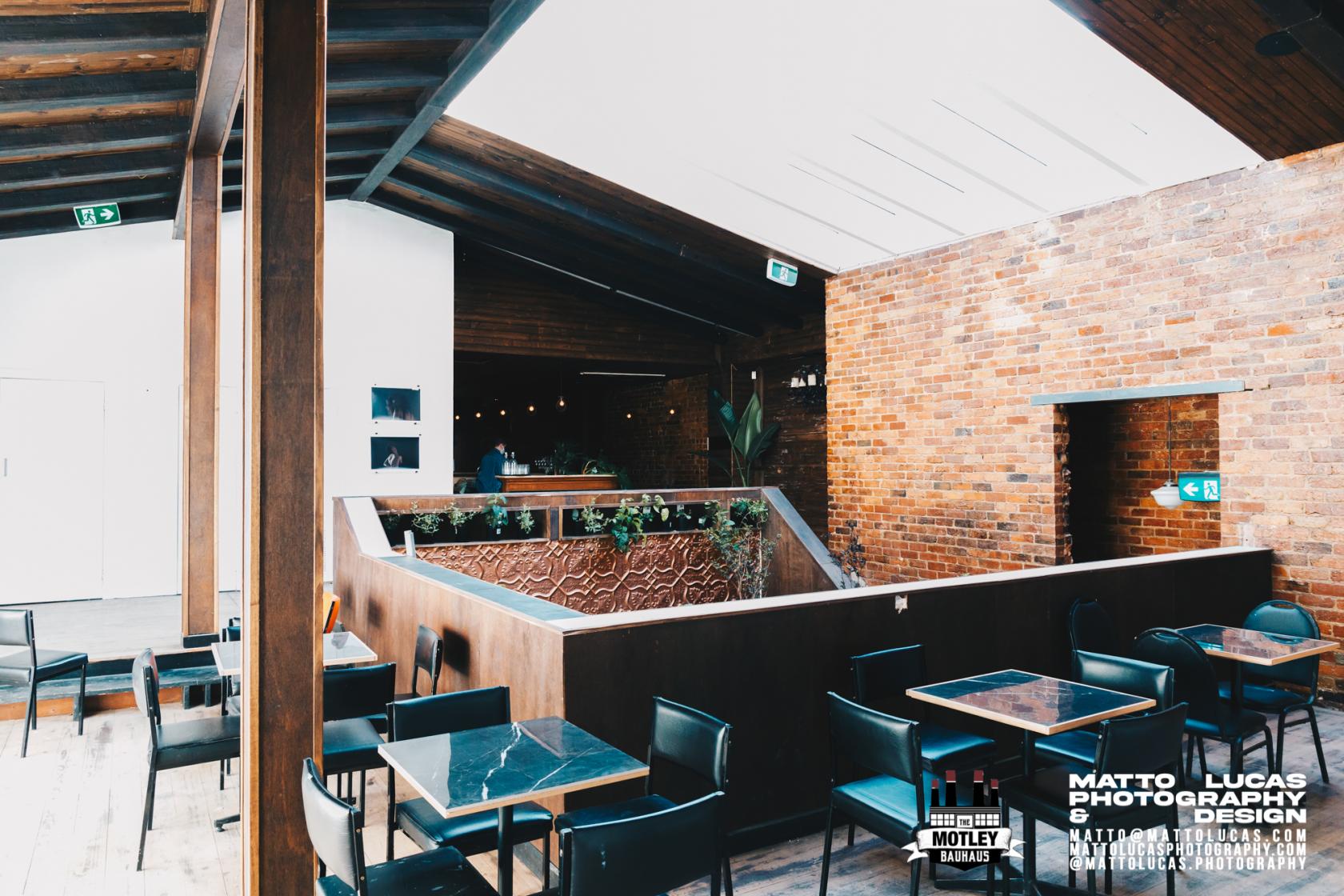 An event space with exposed brick walls, dark wood beams, and black tables at The Motley Bauhaus.