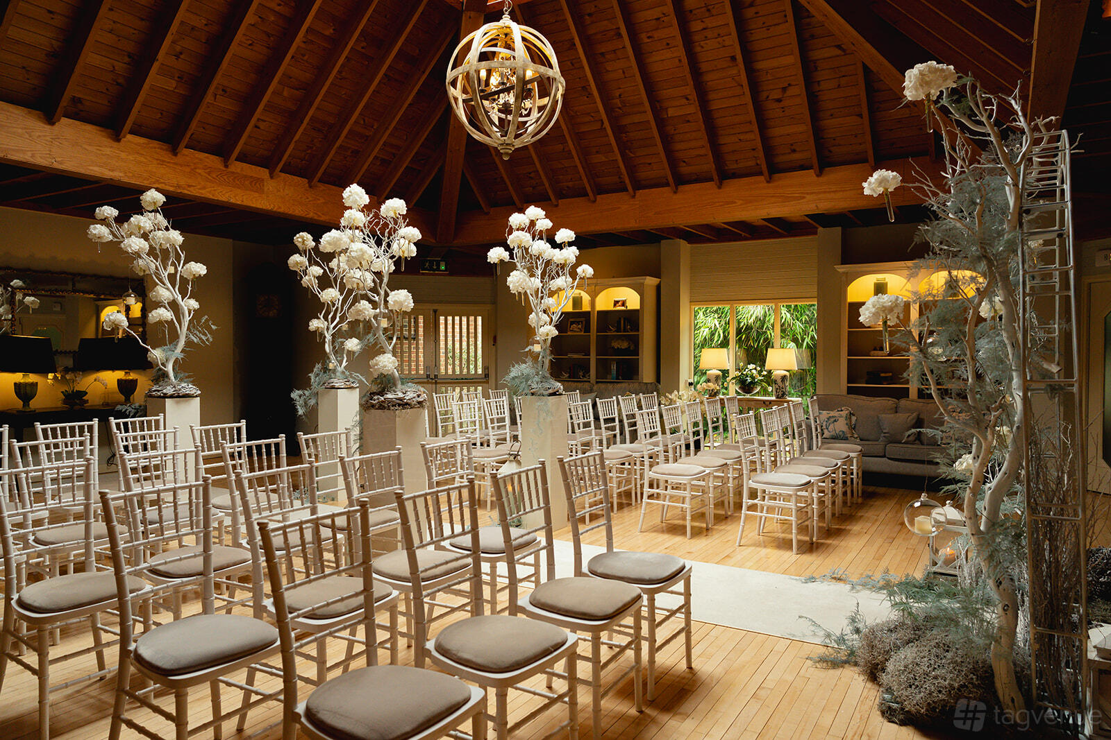A hotel lounge with wooden vaulted ceilings, neutral chairs arranged for a ceremony, and tall floral arrangements at Careys Manor Hotel & Spa.