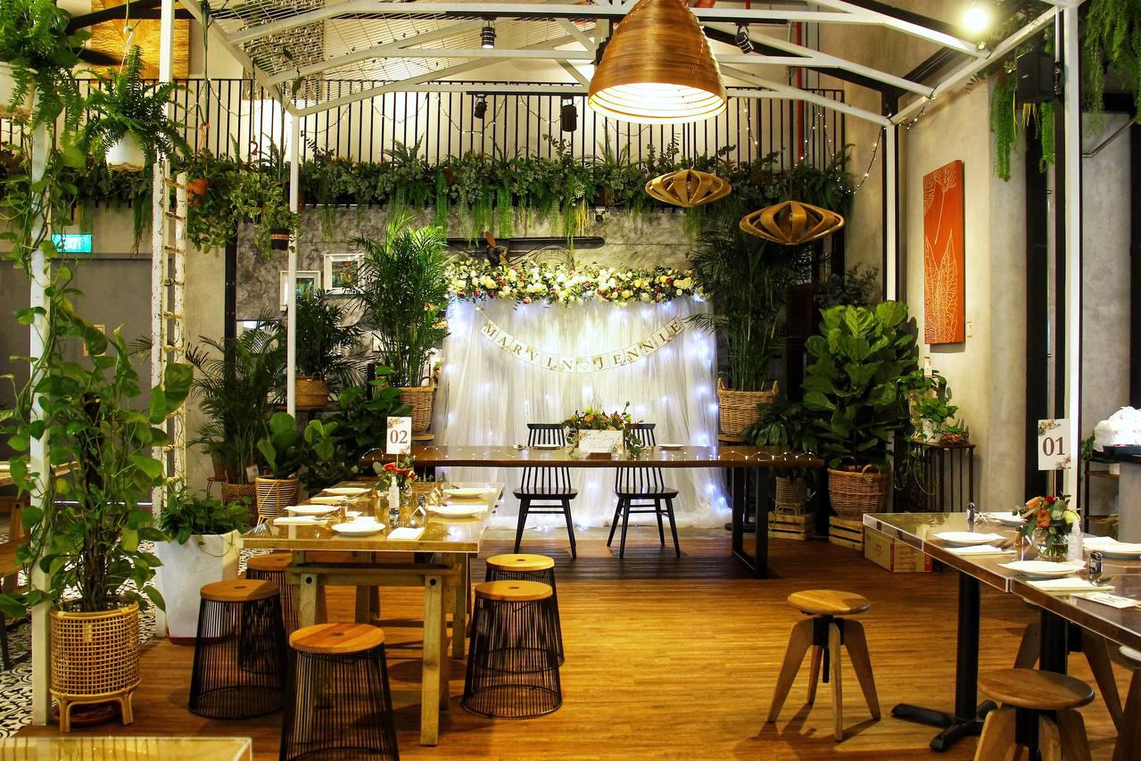 A cafe with wooden tables, stools, lush greenery, and string lights on a decorative backdrop at Knots Cafe and Living (Pasir Panjang).
