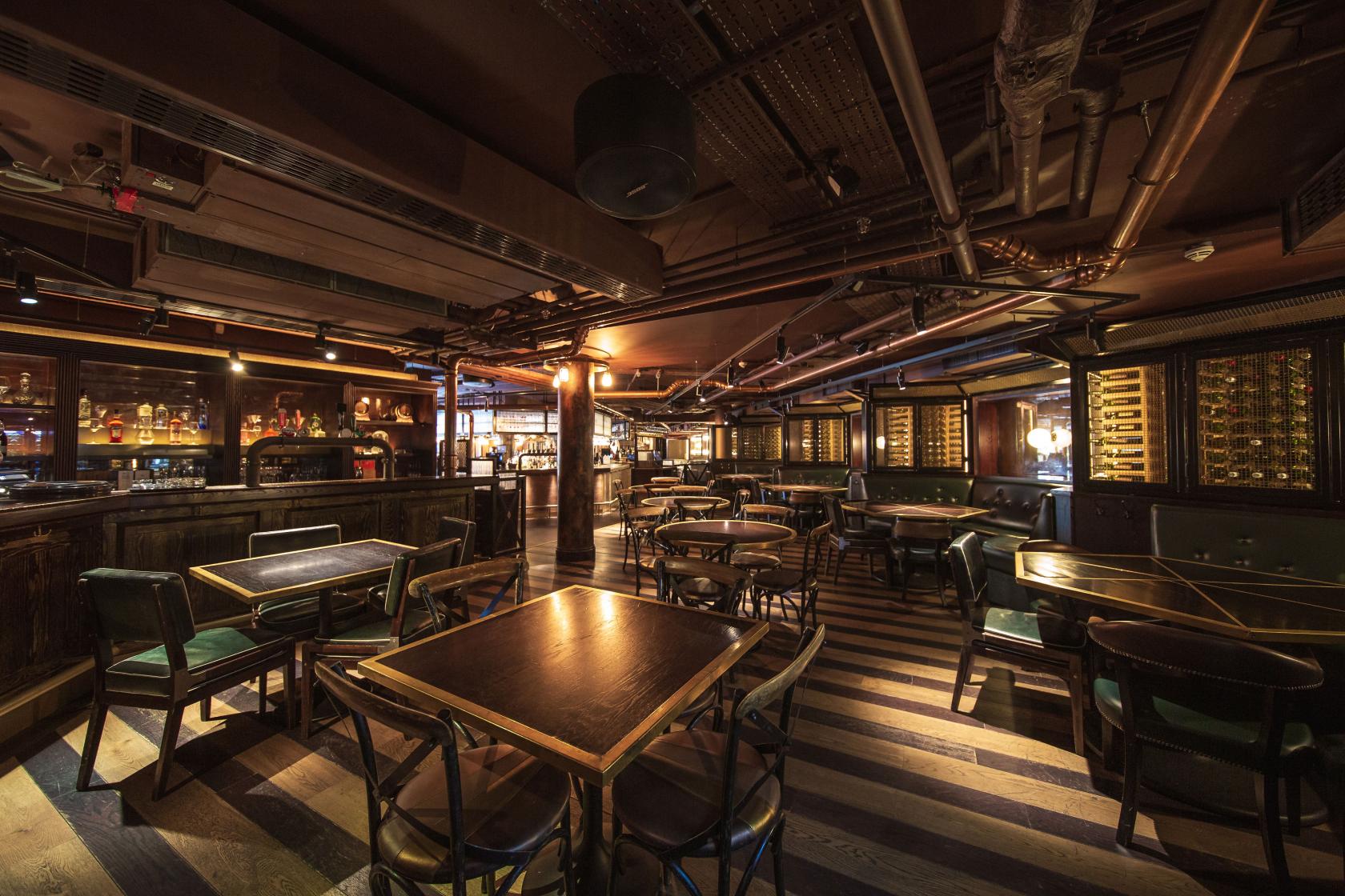 A cocktail bar with dark wood tables, ambient lighting, and an open ceiling at The Botanist Broadgate Circle.