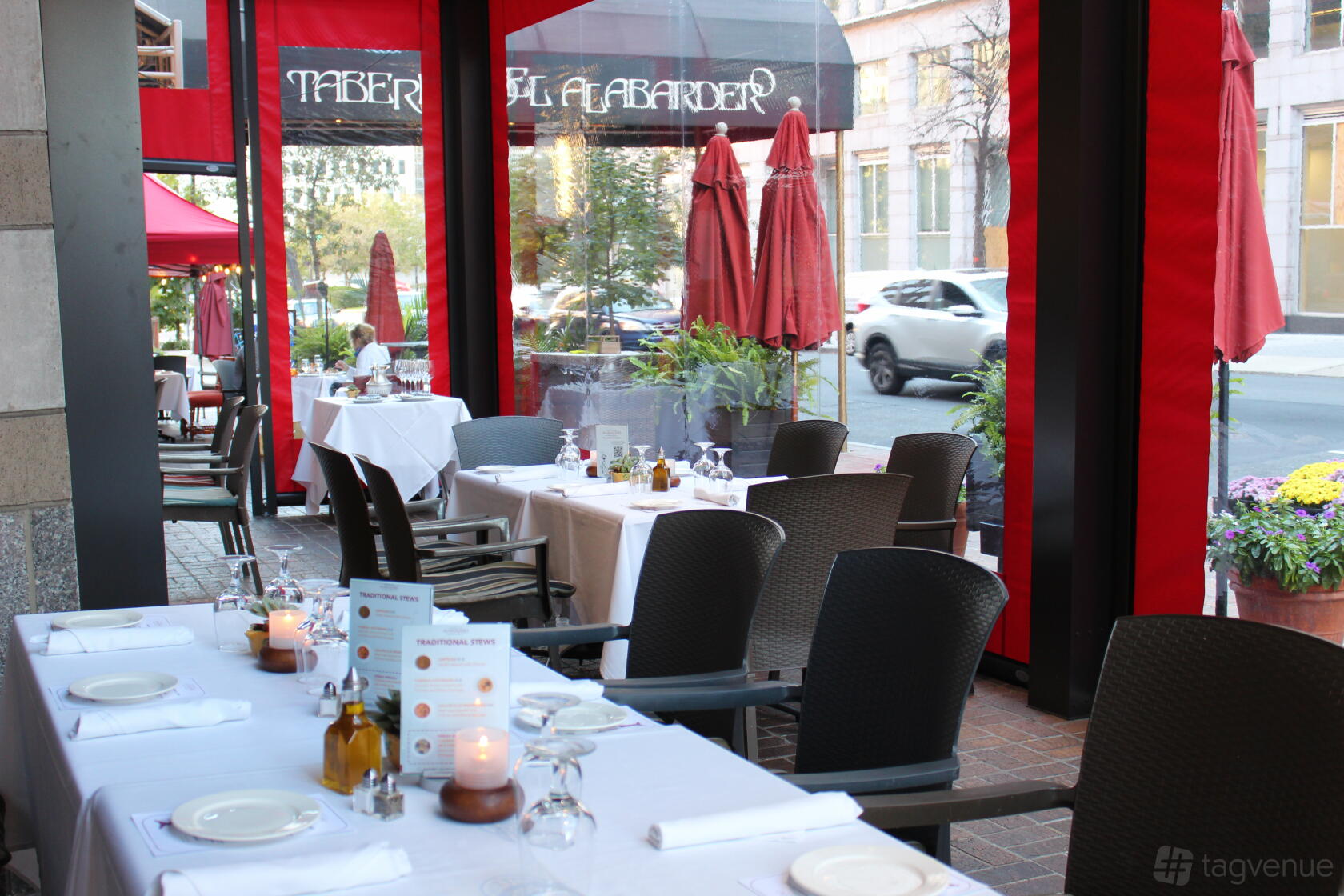 A restaurant patio with white tablecloths, menus, glassware, and red umbrellas at Taberna Del Alabardero.