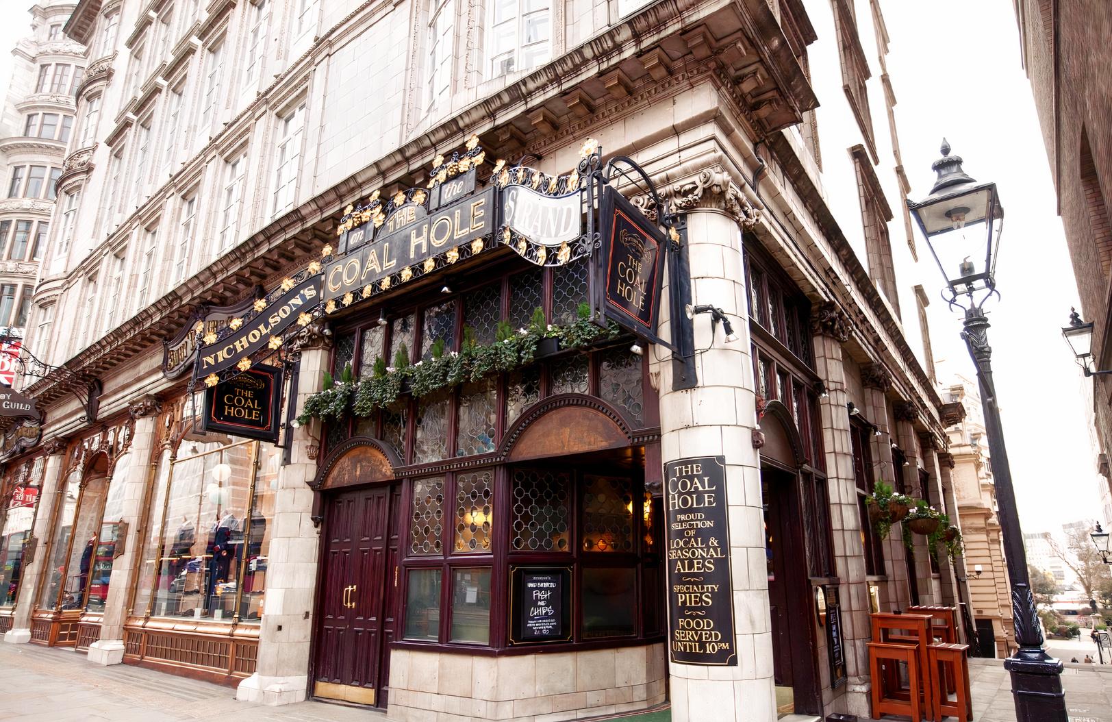 A historic pub exterior with ornate signage, arched windows, and hanging greenery at The Coal Hole.