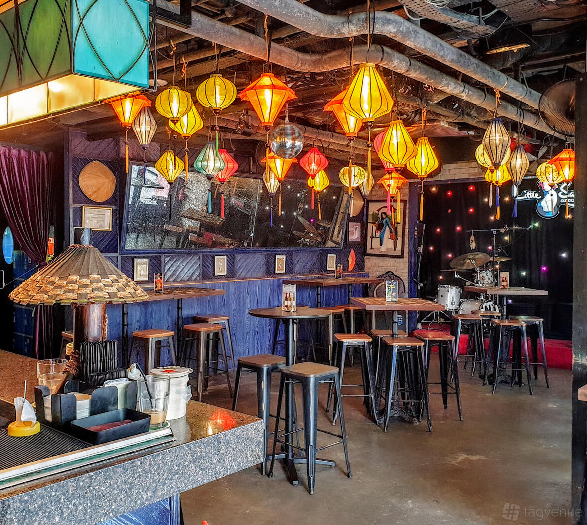 A restaurant with colorful hanging lanterns, high tables with stools, and a small stage with instruments at Little Saigon.