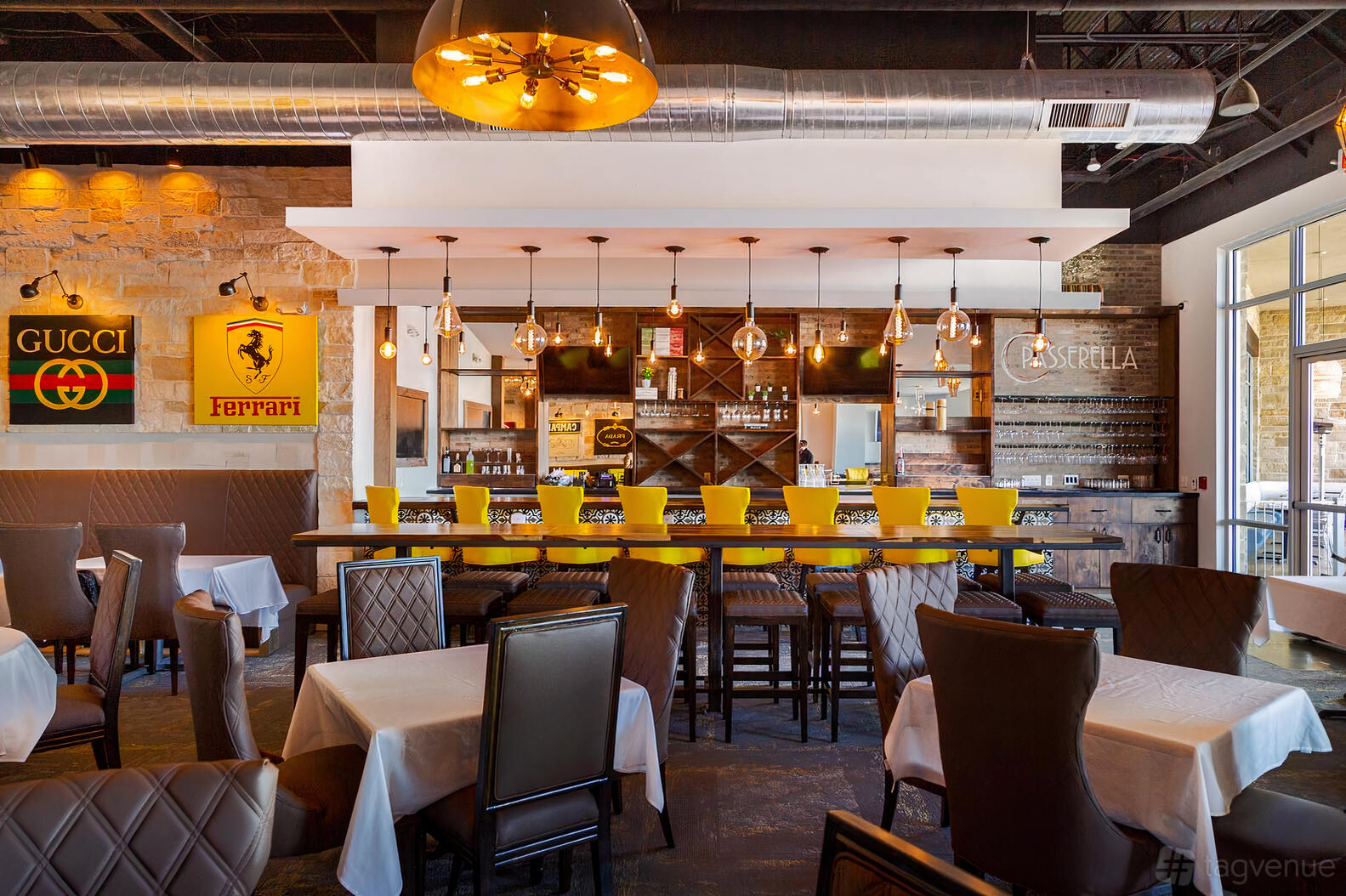 A restaurant with leather chairs, white tablecloths, exposed ductwork, and a bar with yellow stools at Passerella.