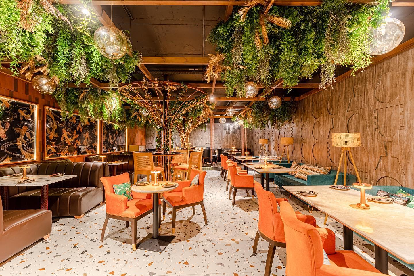 A restaurant with hanging greenery, terrazzo floors, orange velvet chairs, and wood-paneled walls at Gura Gura.