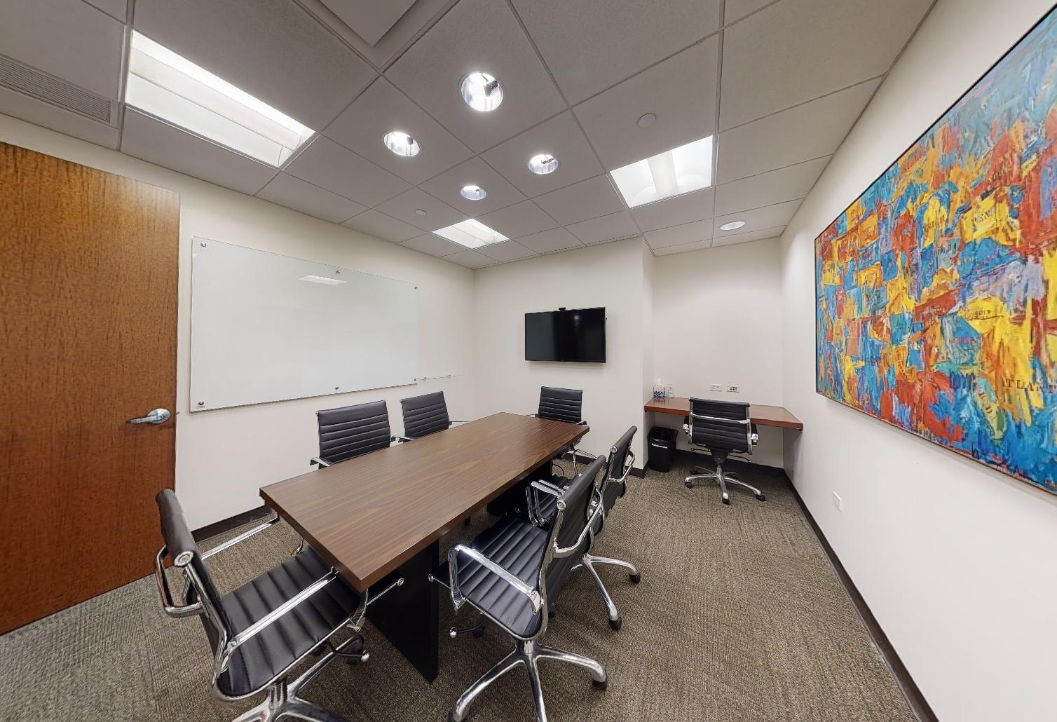 A conference room with a rectangular table, black chairs, wall-mounted TV, and colorful abstract art at Corporate Suites - Lexington Avenue.