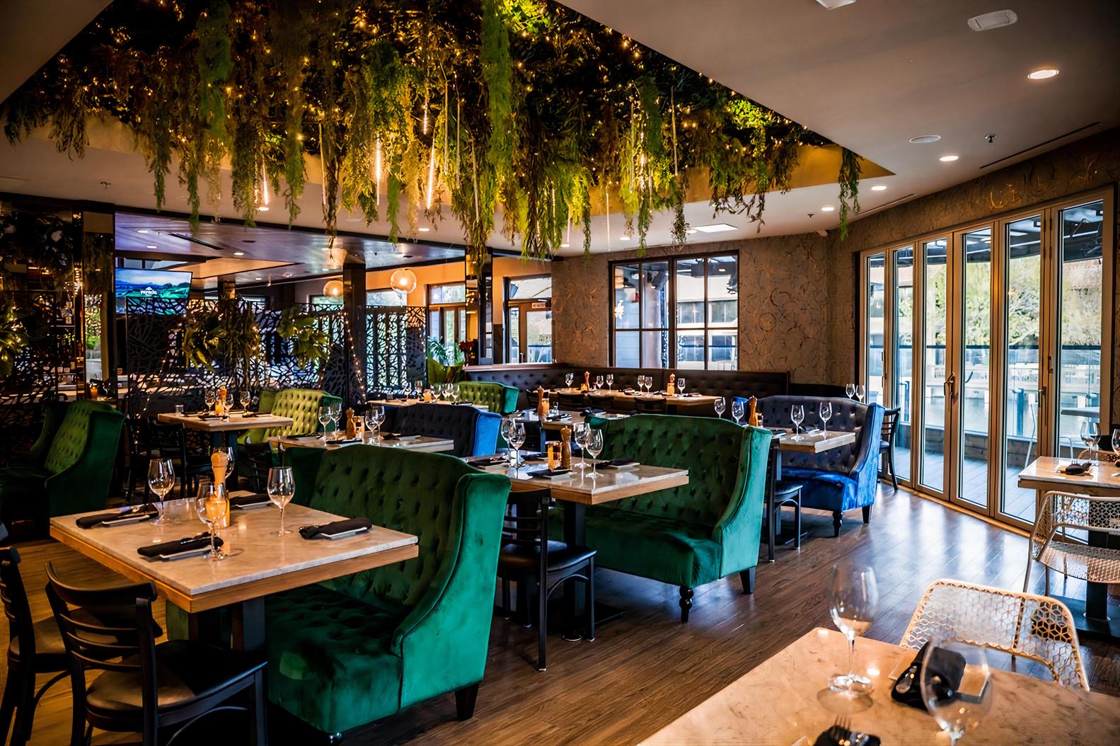 A restaurant dining room with green velvet booths, marble tables, and hanging greenery at TK's.