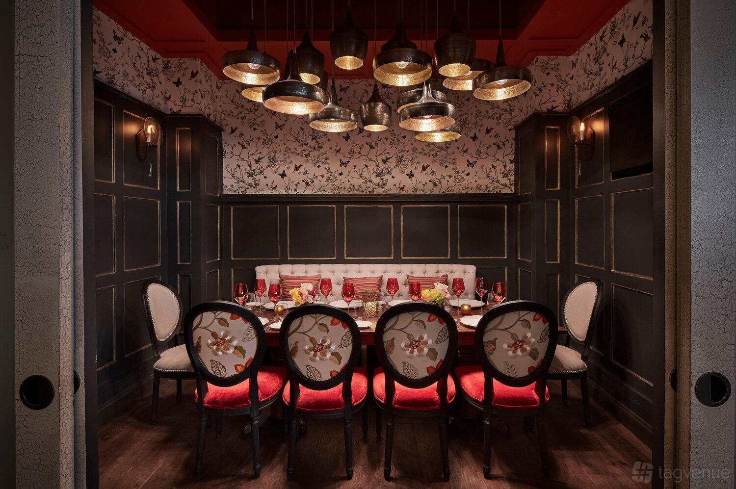 A restaurant dining room with floral wallpaper, pendant lighting, and a long table with upholstered chairs at Sfoglina Downtown.