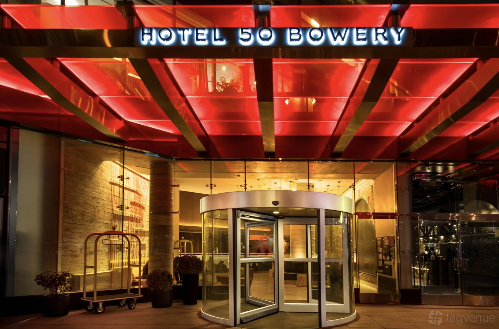 A hotel entrance with a glass canopy, illuminated signage, and a revolving door at Hotel 50 Bowery.