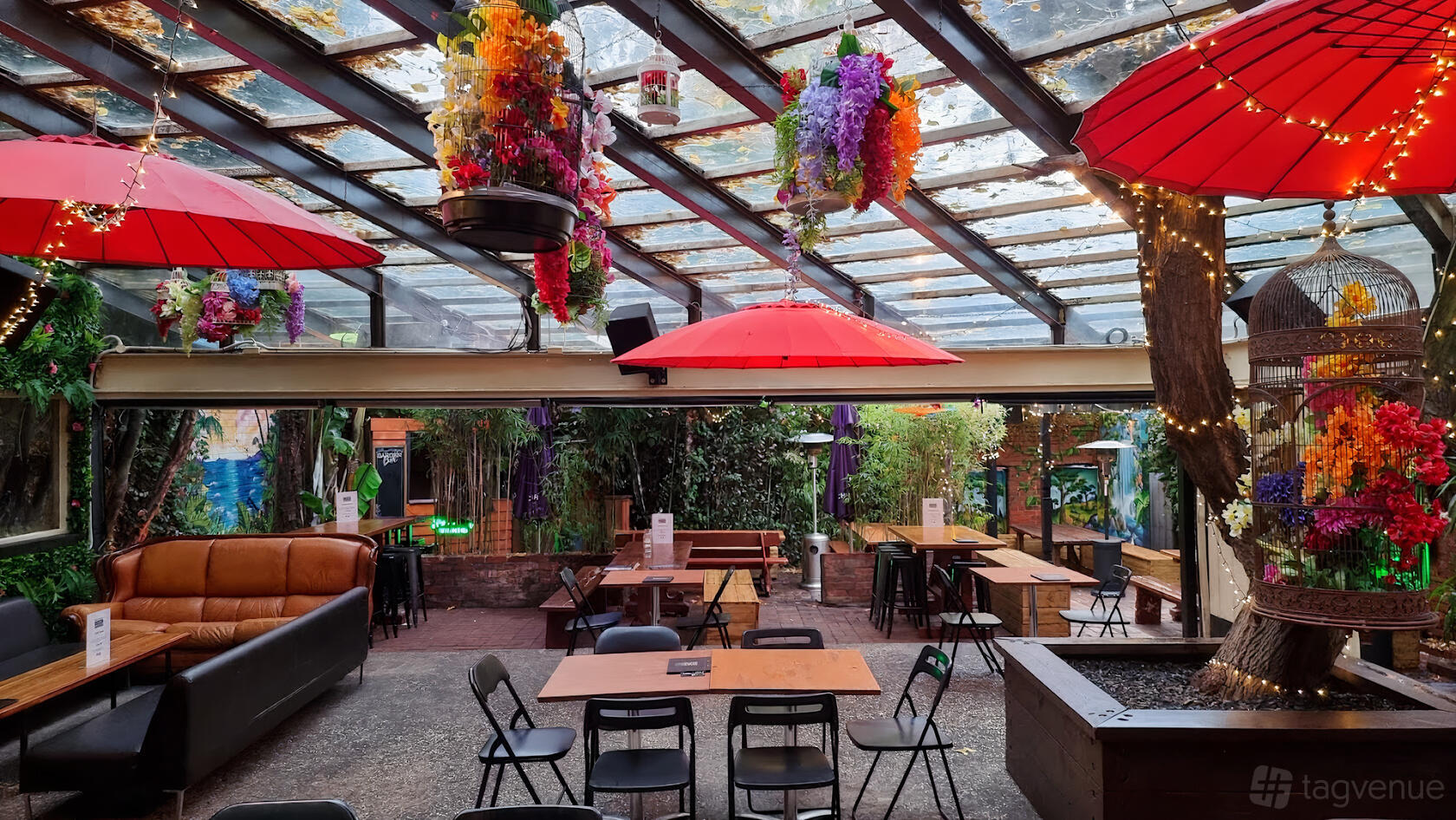 An indoor garden with hanging flowers, red umbrellas, and wooden tables at The Fitzroy Beer Garden.