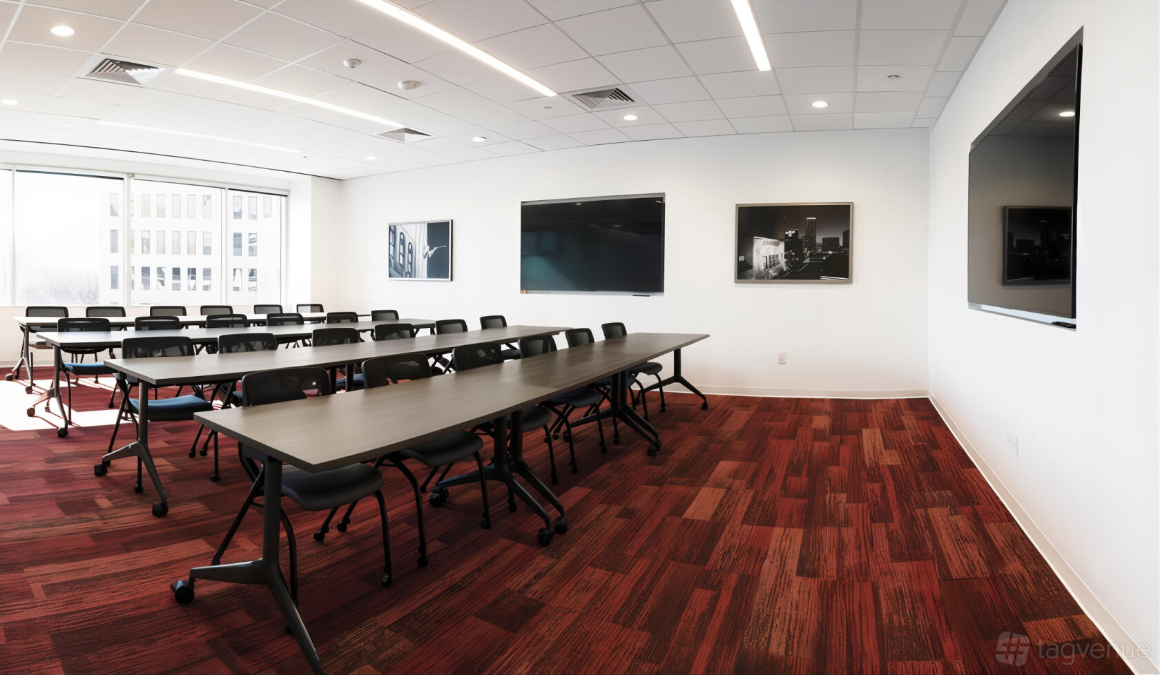 A classroom with rows of black chairs, rectangular tables, wall-mounted screens, and red patterned carpet at CityCentral - Fort Worth.