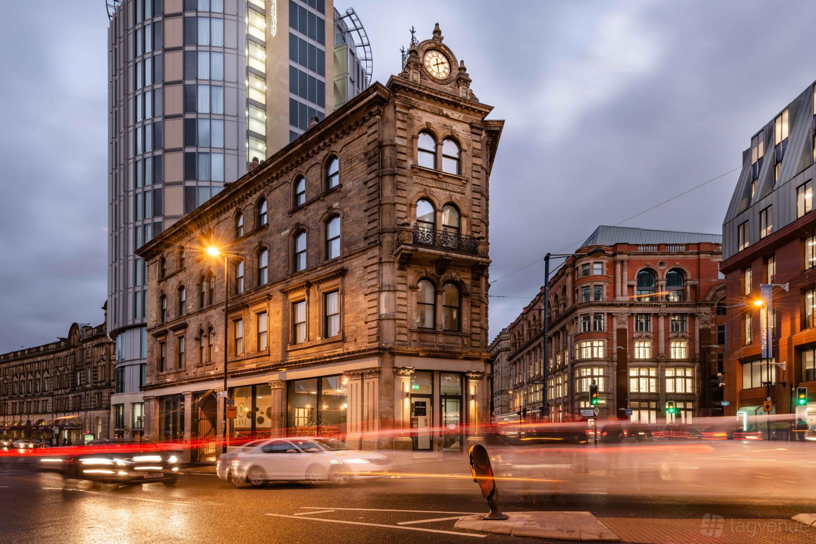 A hotel with a historic stone facade and clock tower next to a modern glass building at Hotel Indigo Manchester - Victoria Station.