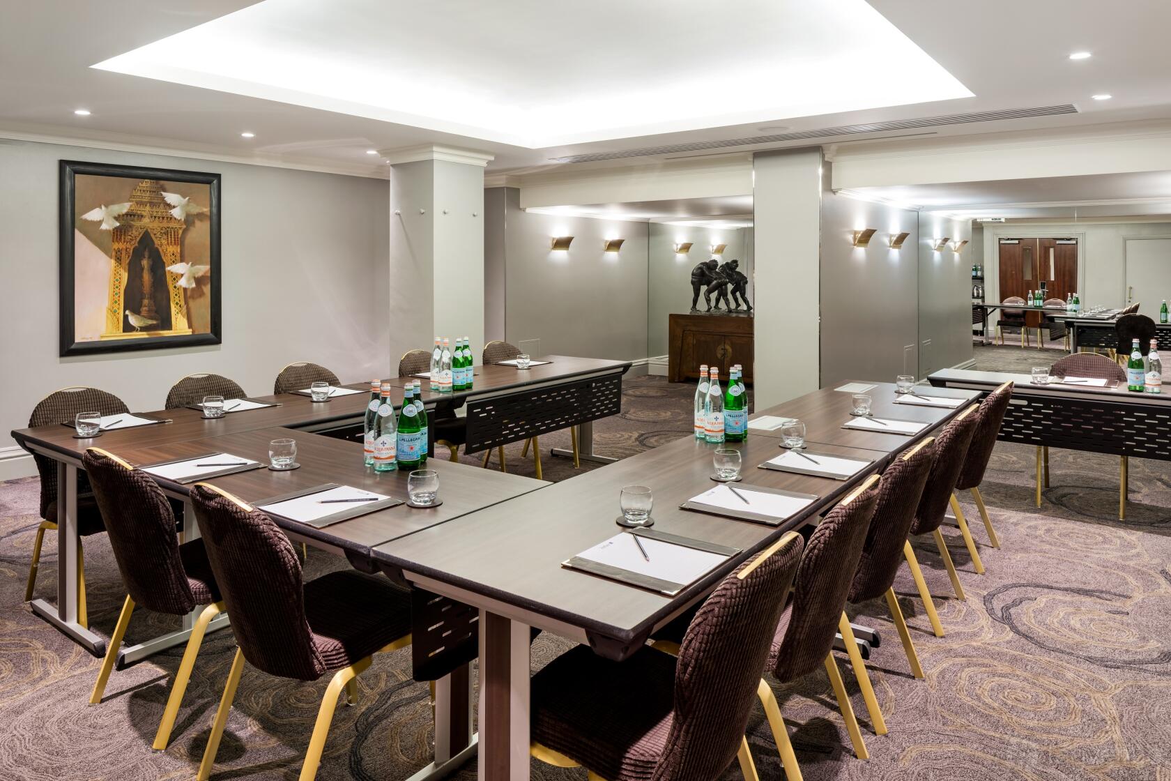 An event space with U-shaped conference tables, cushioned chairs, bottled water, and notepads at Radisson Blu Hotel, London Euston Square.