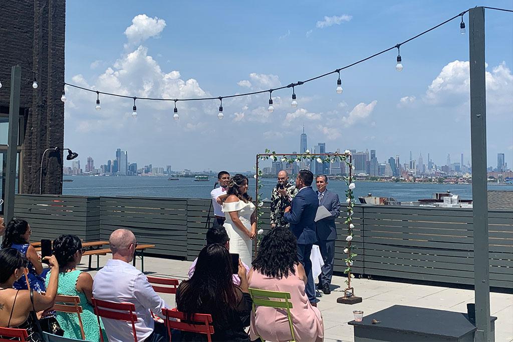 A rooftop venue with string lights, colorful chairs, and waterfront city skyline views at Sunset Park Rooftop.