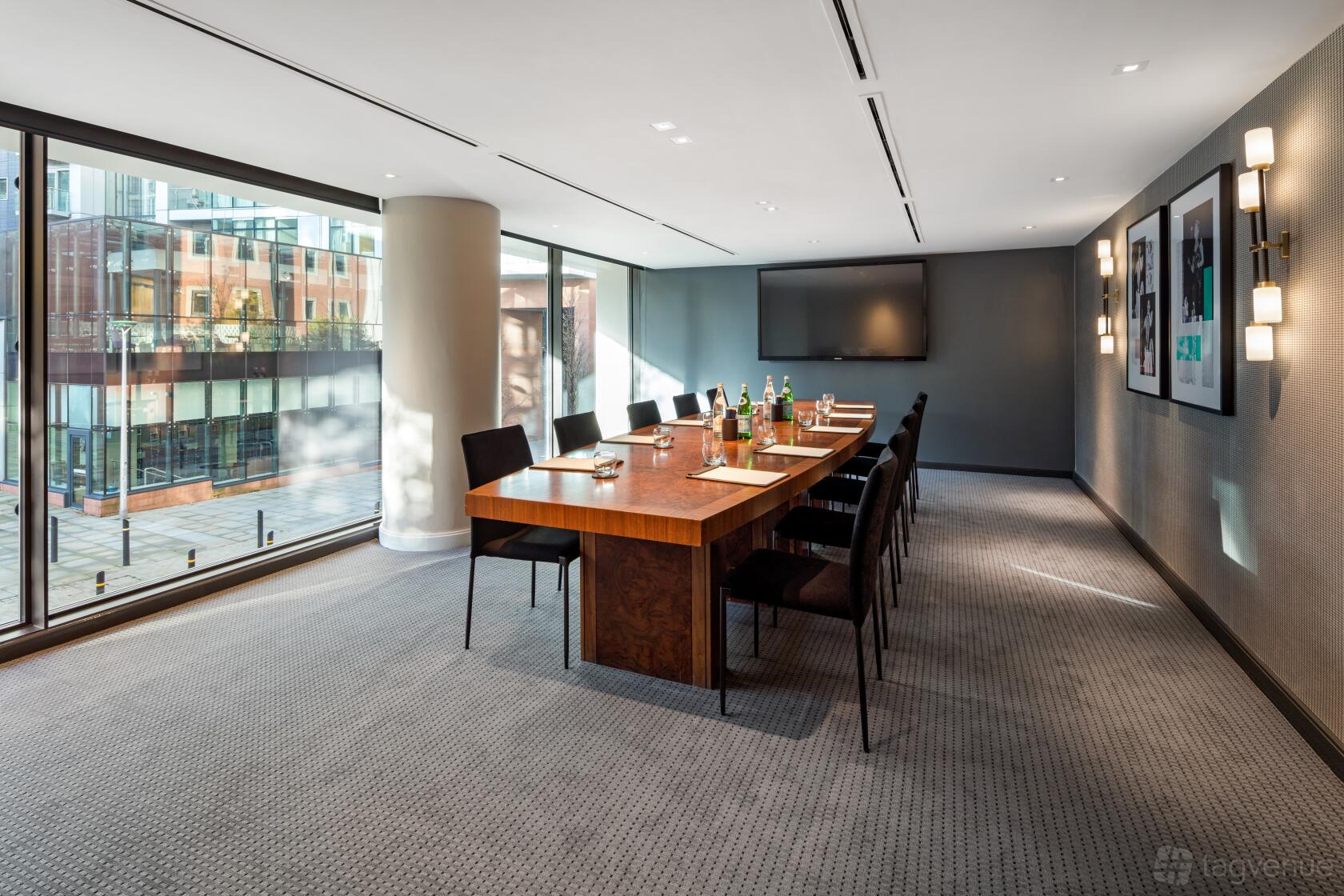 A hotel meeting room with floor-to-ceiling windows, a wooden conference table, and wall-mounted lights at The Edwardian Manchester.