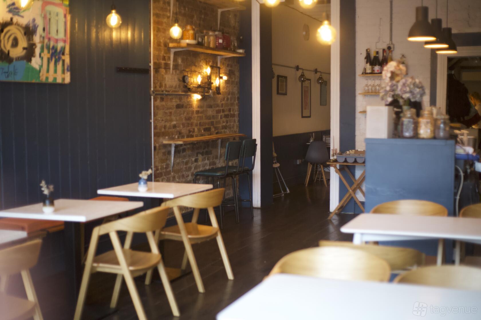 A restaurant with exposed brick walls, wooden chairs, white tables, and hanging pendant lights at Omni.