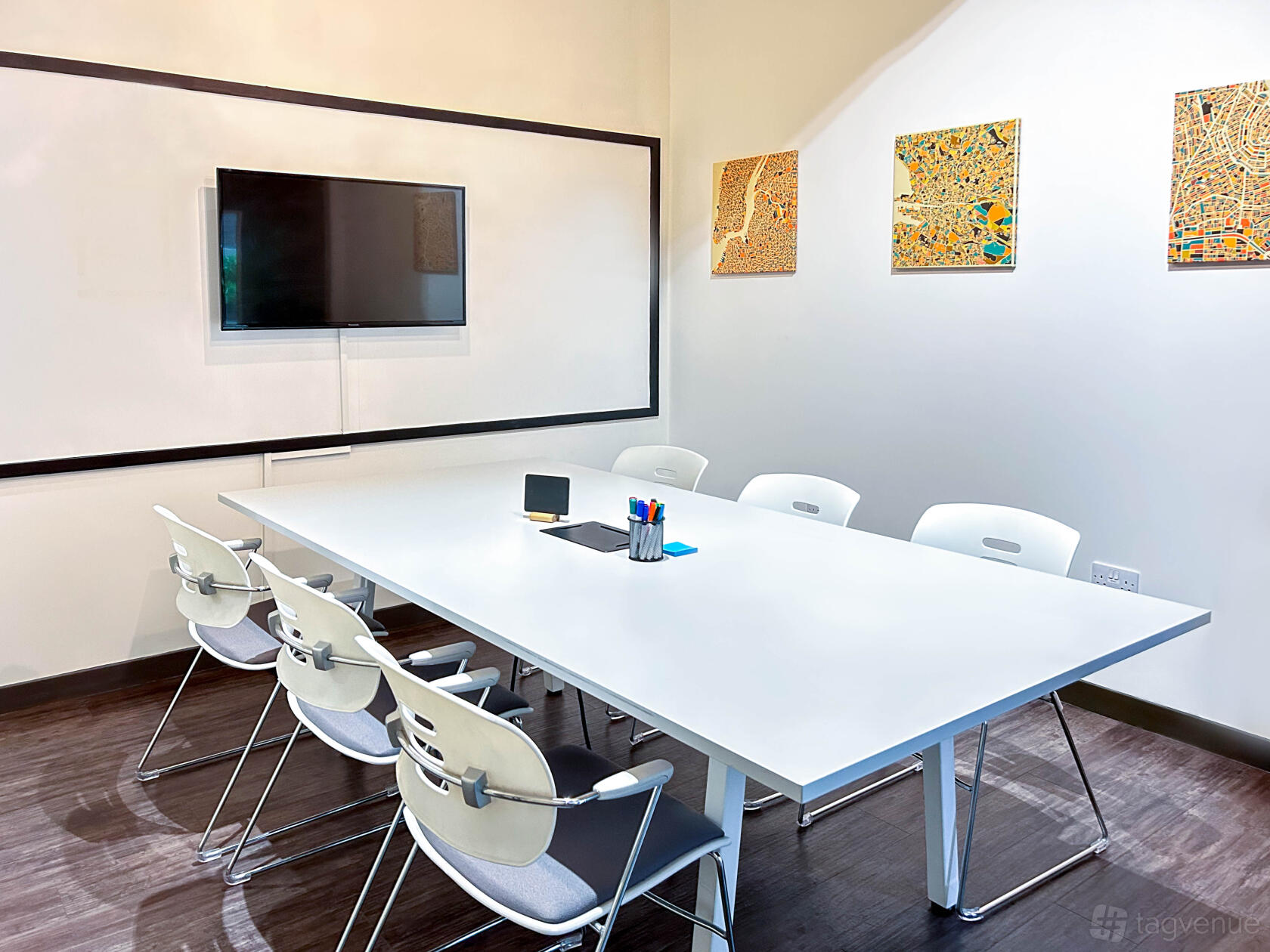 A meeting room with a white conference table, white chairs, wall-mounted screen, and map artwork at Moneypenny Workhub.