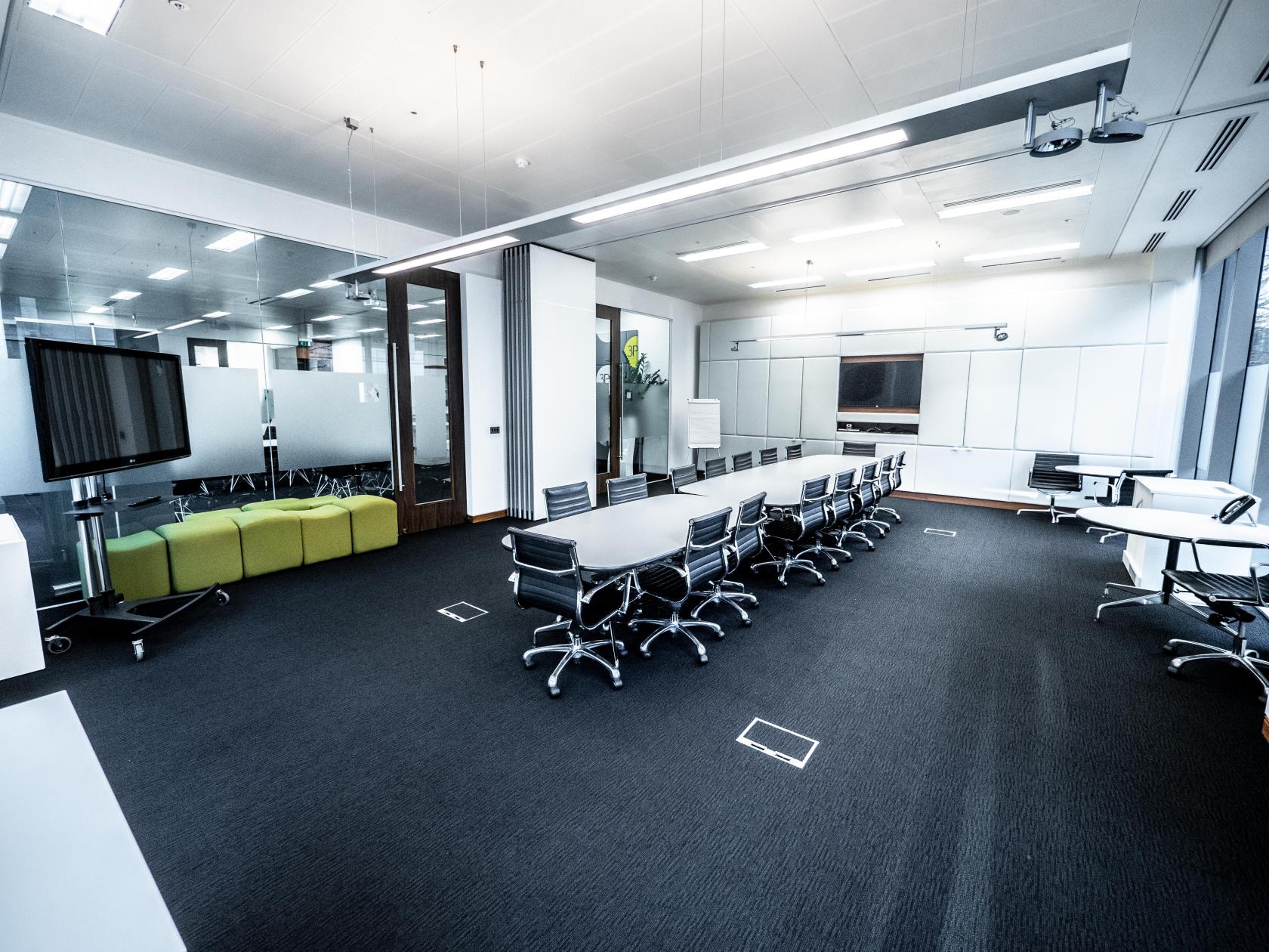 A boardroom with a long conference table, black chairs, glass walls, and a large monitor at Event Space at 3PB Birmingham.