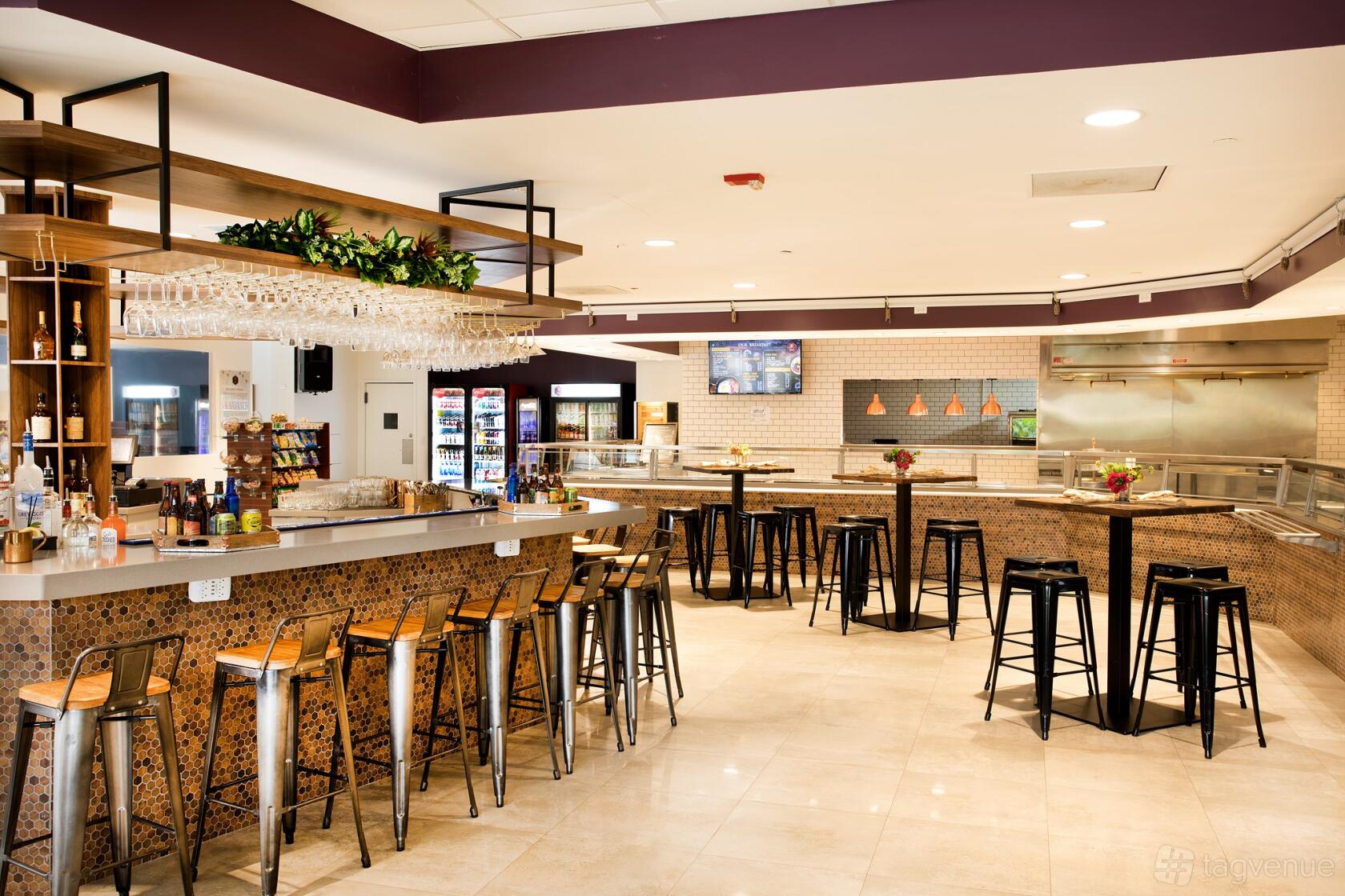 A restaurant with a tiled bar, hanging glassware, high-top tables, and open kitchen at Stela's Kitchen & Bar.