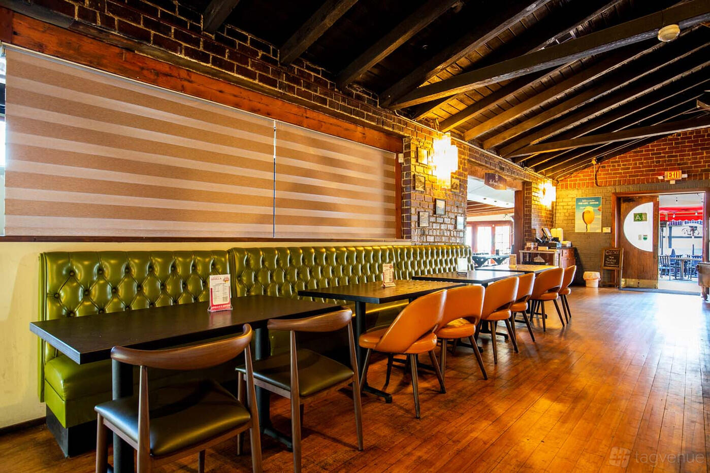 A restaurant with exposed brick walls, wood flooring, and olive green banquette seating at Ivanhoe Restaurant & Bar.