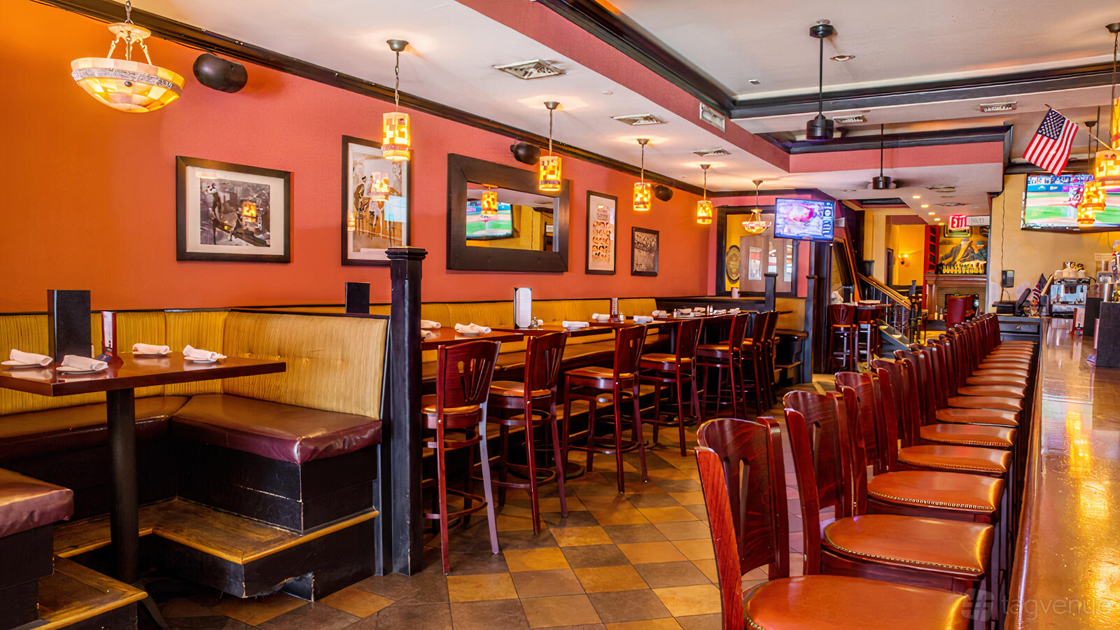 A bar with wooden high-top tables, cushioned chairs, pendant lighting, and framed wall art at Gossip Bar & Restaurant.
