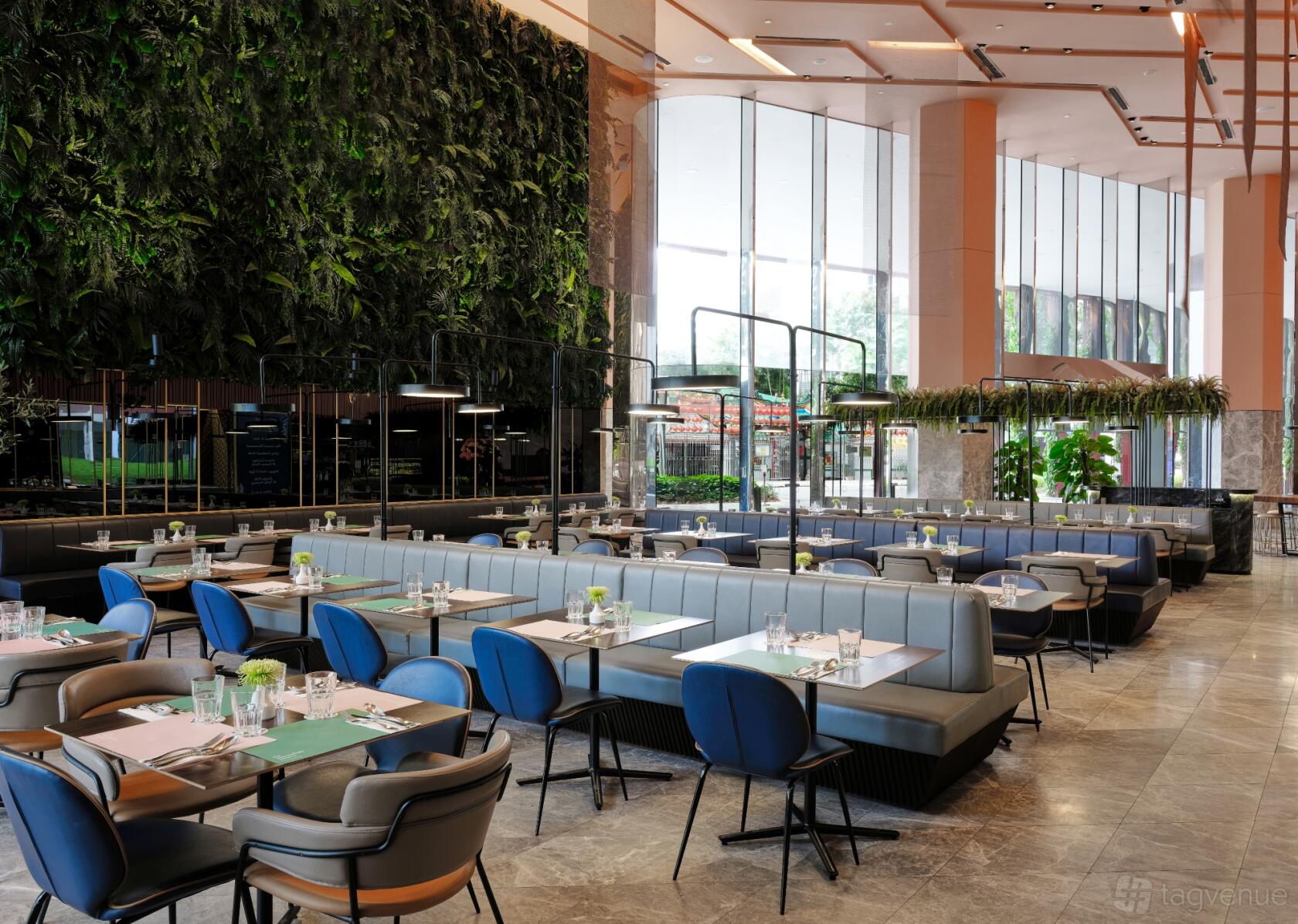 A restaurant with blue upholstered chairs, booth seating, marble flooring, and a large green wall at The Marmalade Pantry Downtown.