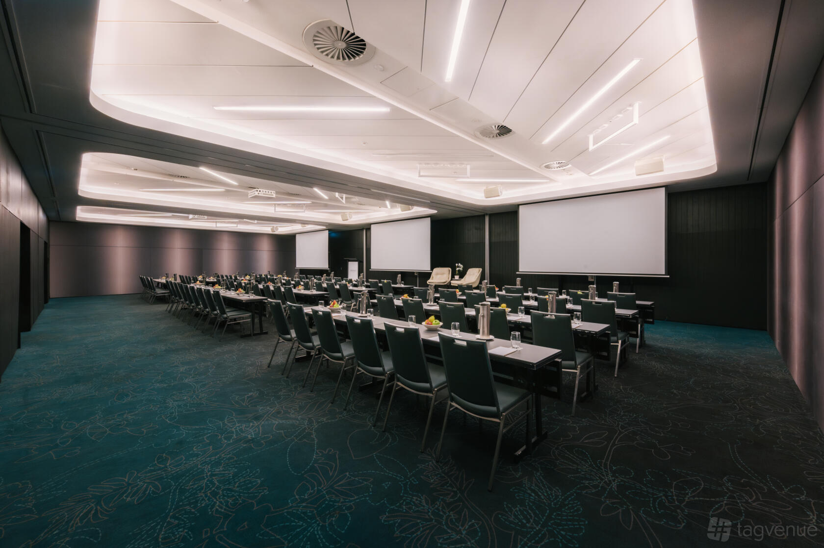 A hotel function room with long conference tables, teal carpet, and ceiling strip lighting at PARKROYAL Darling Harbour, Sydney.