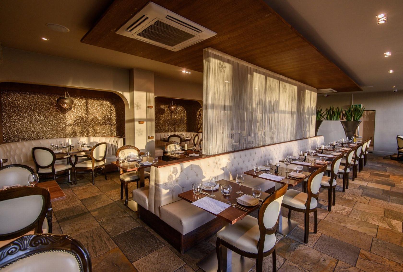 A restaurant dining room with tufted banquette seating, elegant chairs, and large windows at The Mint Room.
