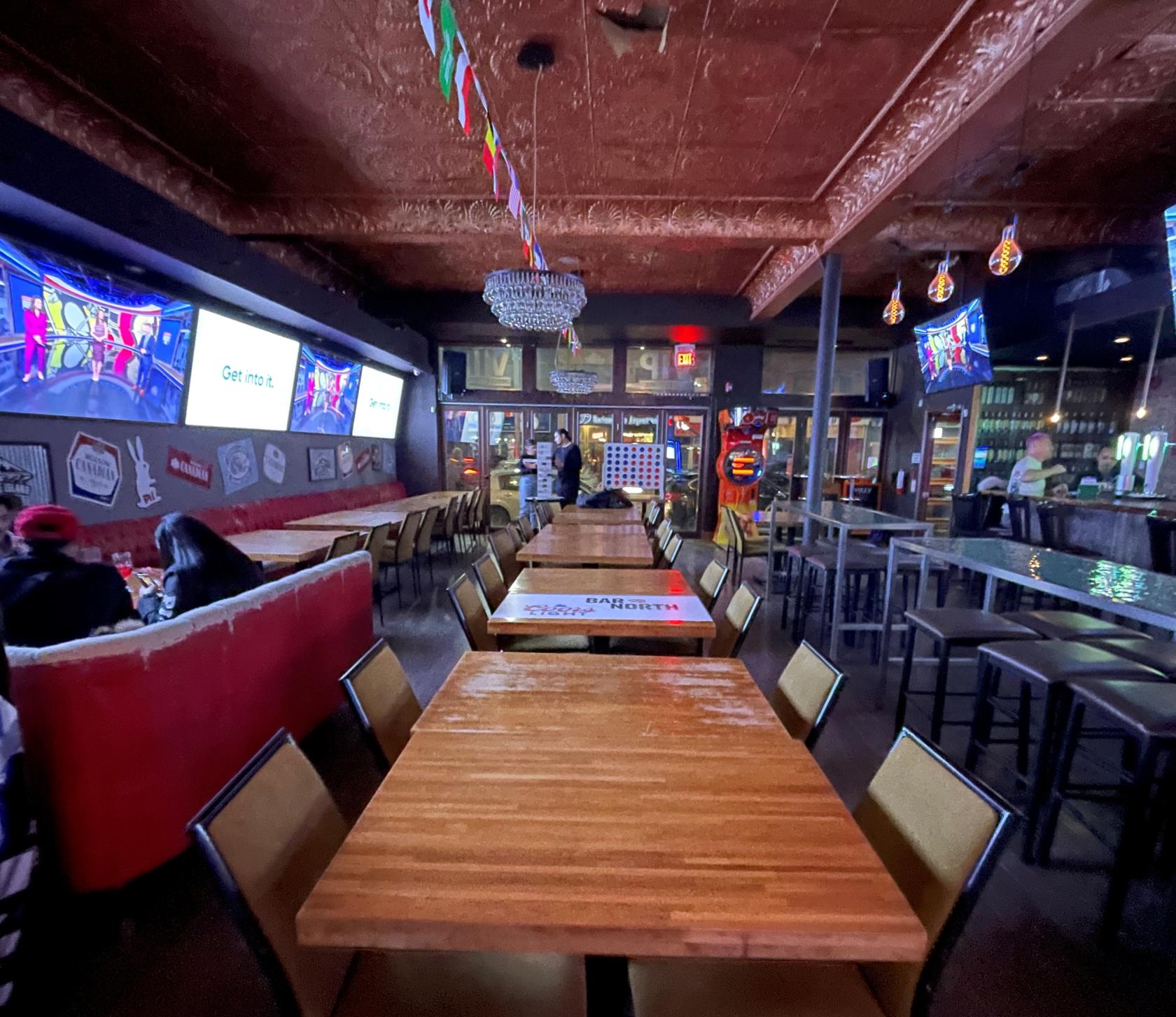 A bar with long wooden tables, high-top seating, multiple TVs, and a chandelier at VIP Billiards & Lounge - Toronto.