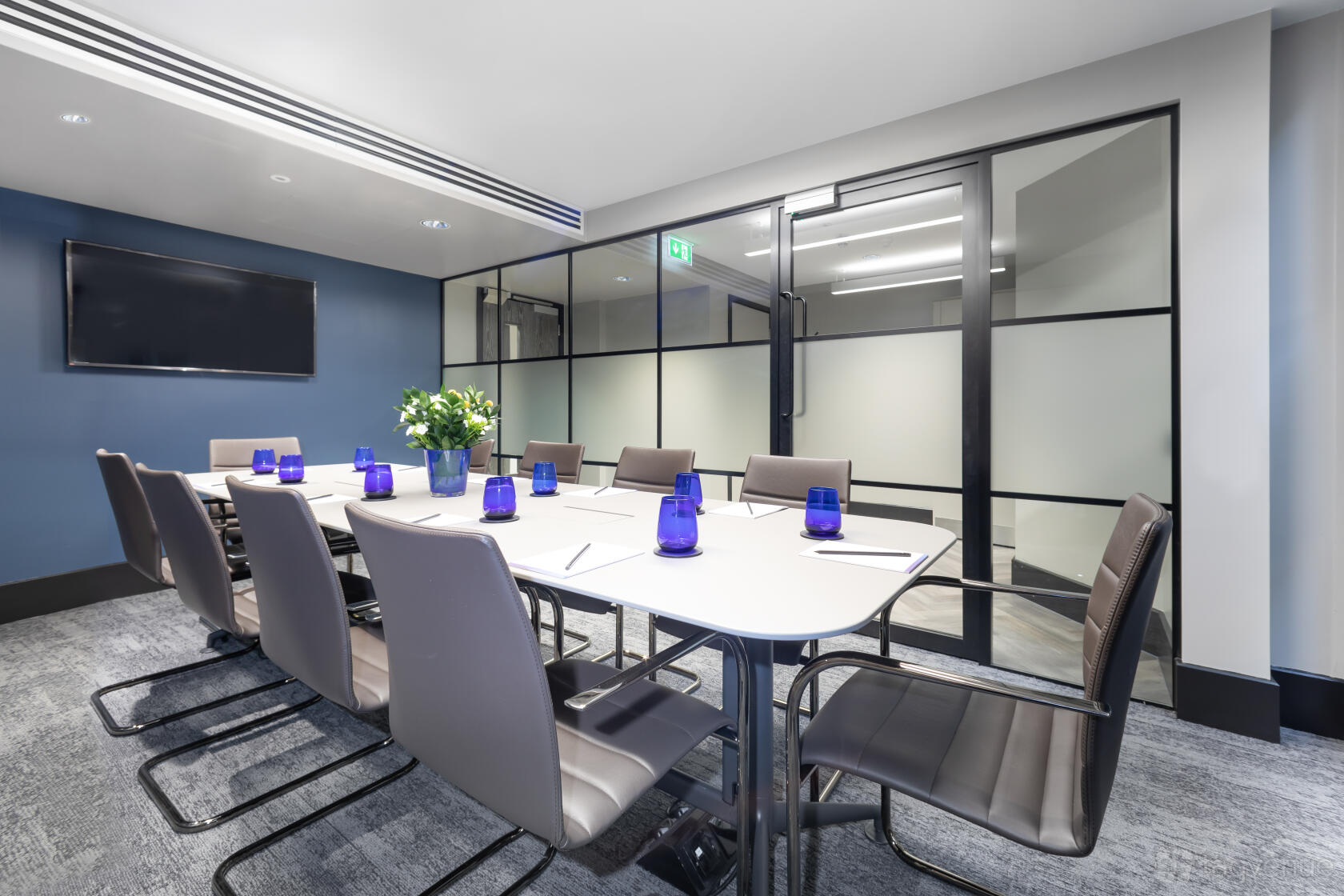 A conference centre room with a long table, grey chairs, blue water glasses, and glass partition walls at Landmark: Park Street, Mayfair, London.