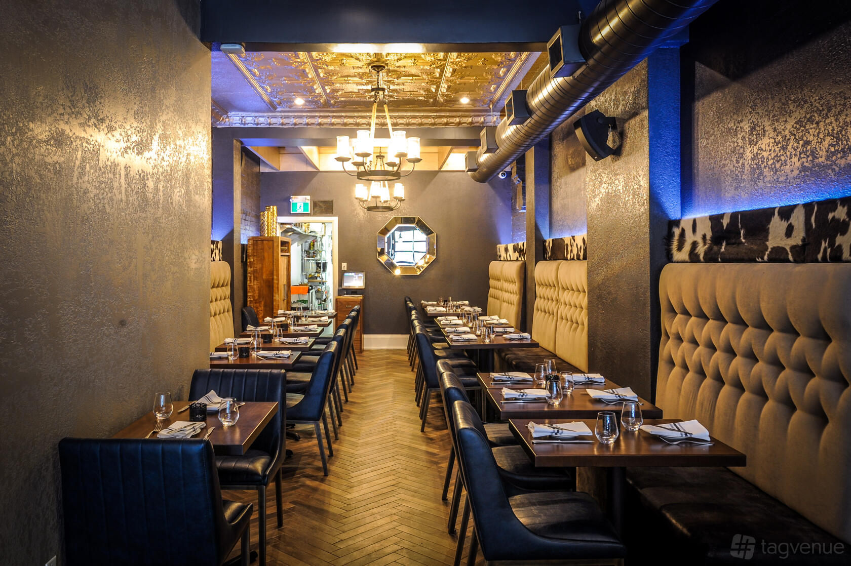 A restaurant with tufted banquette seating, wood tables, and metallic ceiling panels at Vos Restaurante Argentino - Lake Shore.