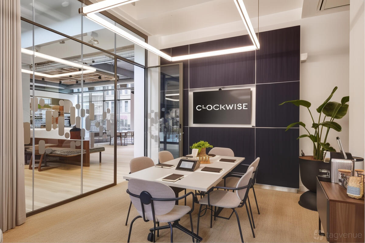 A boardroom with a rectangular meeting table, modern chairs, a wall-mounted screen, and glass partition at Clockwise Manchester.